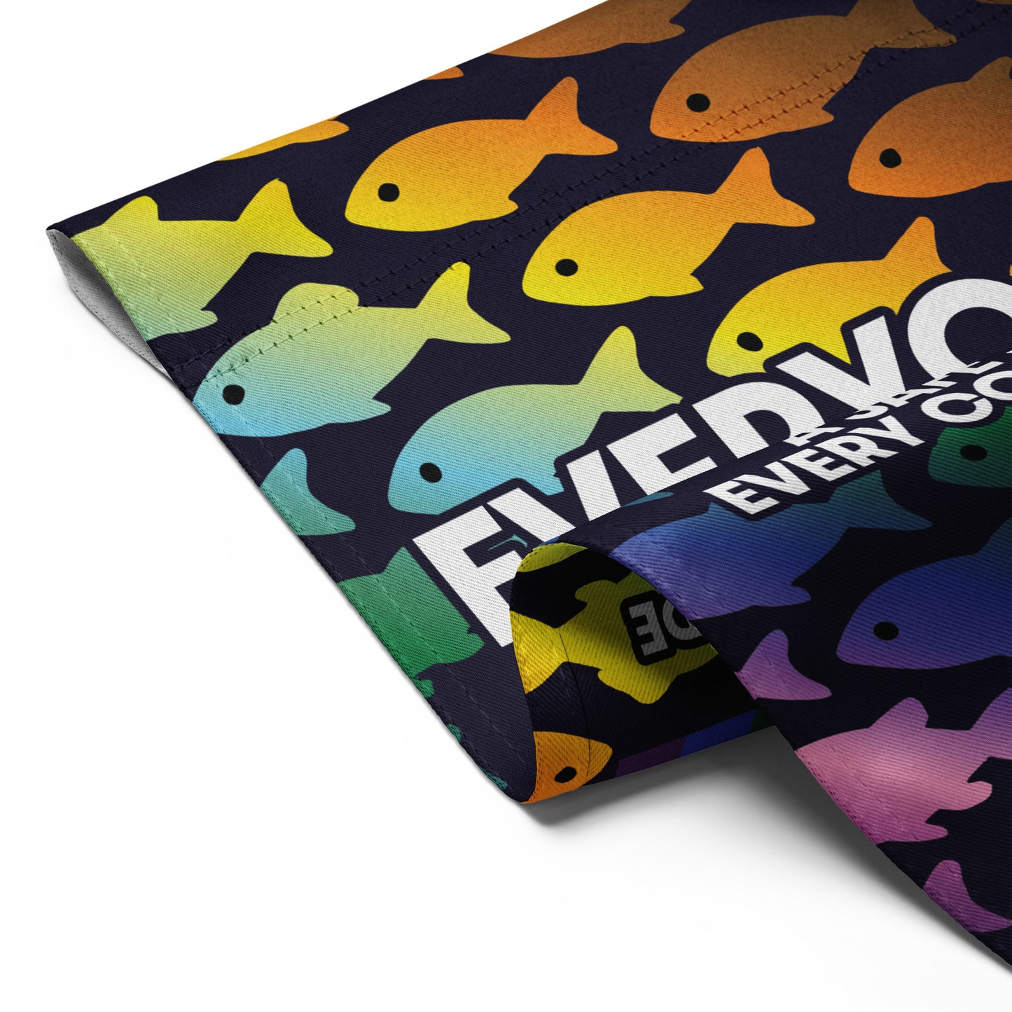 Close-up of the “Everyone Is Welcome Here” rainbow fish pride flag with curled corner showing bright colors and bold text.