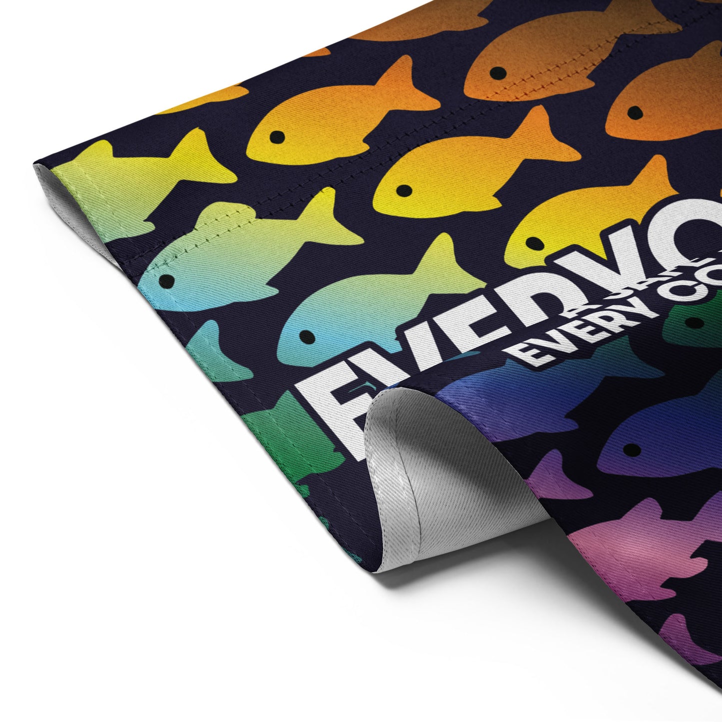 Close-up of the “Everyone Is Welcome Here” rainbow fish pride flag with curled corner showing bright colors and bold text.