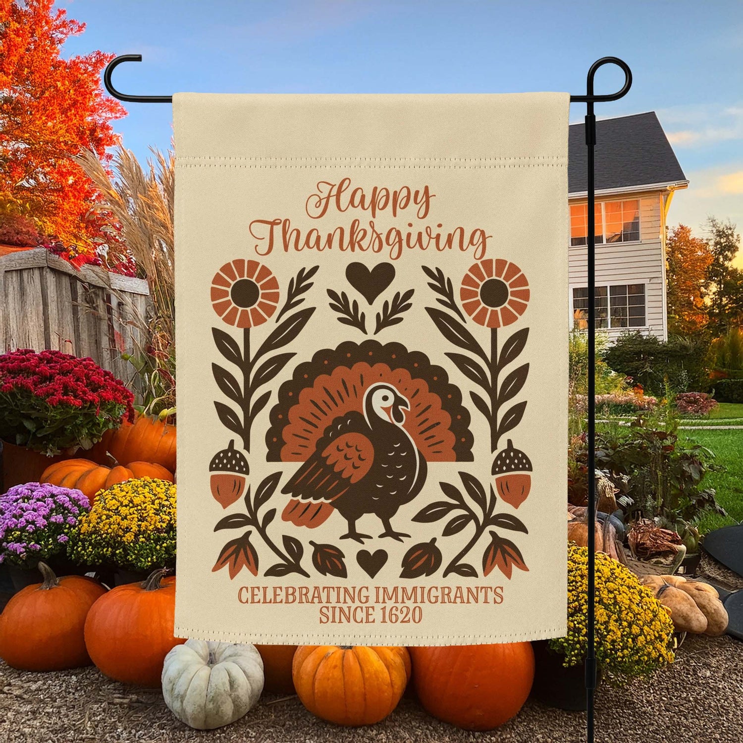 “Happy Thanksgiving – Celebrating Immigrants Since 1620” garden flag with folk-art style turkey, flowers, and leaves, displayed outdoors among pumpkins and fall décor.