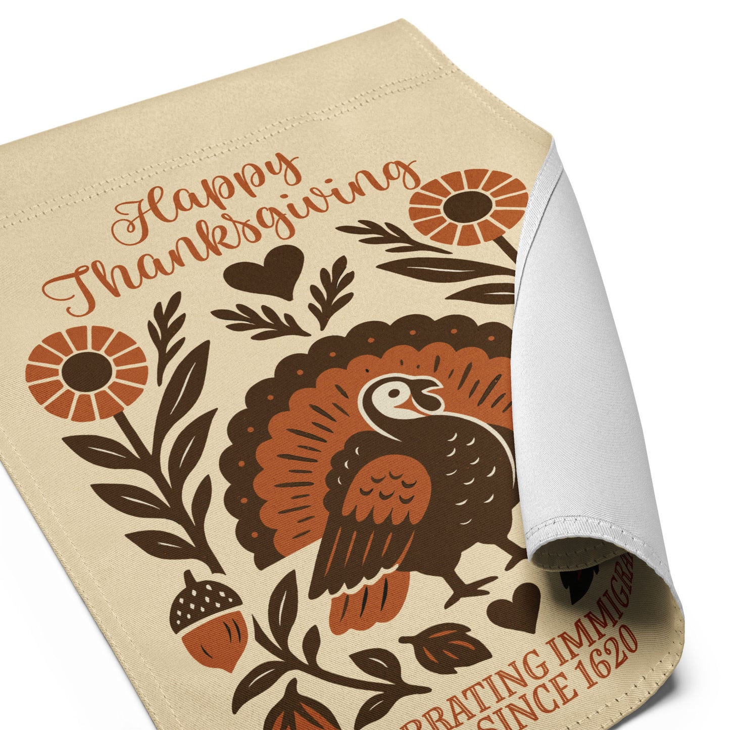Angled view of the “Happy Thanksgiving – Celebrating Immigrants Since 1620” garden flag with curled fabric corner highlighting the folk-art turkey and floral elements.