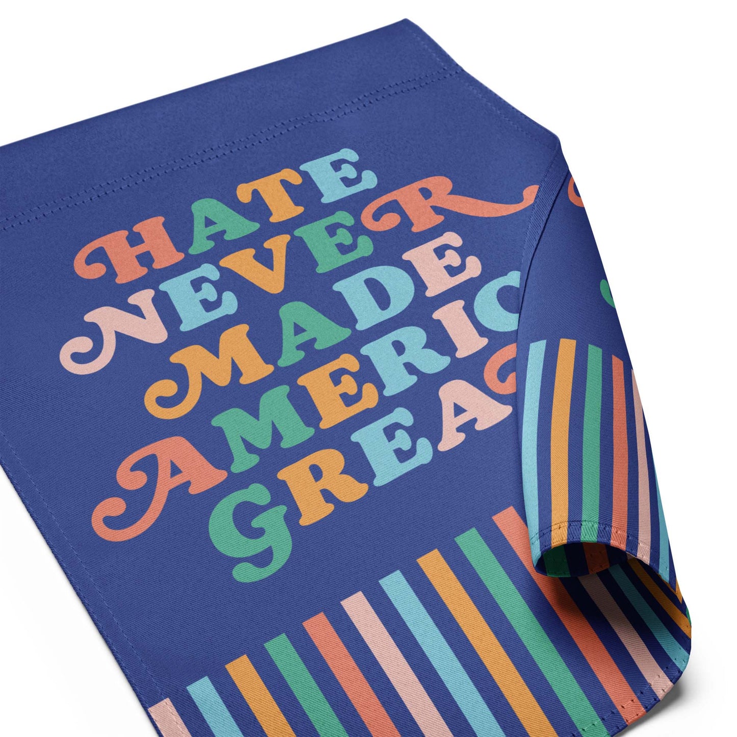 Close-up of the “Hate Never Made America Great” retro-style garden flag with curled corner and multicolor striped base.