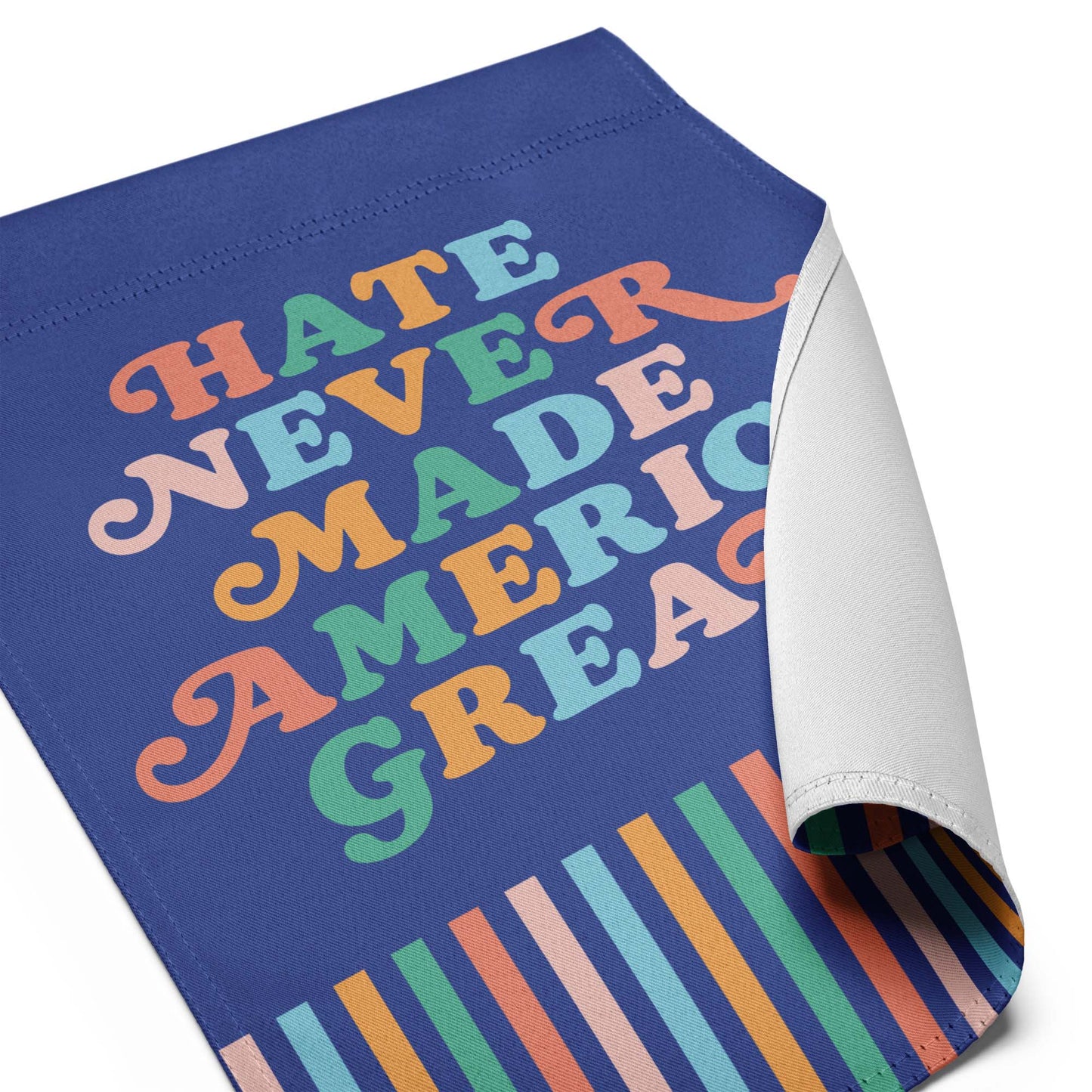 Close-up of the “Hate Never Made America Great” retro-style garden flag with curled corner and multicolor striped base.