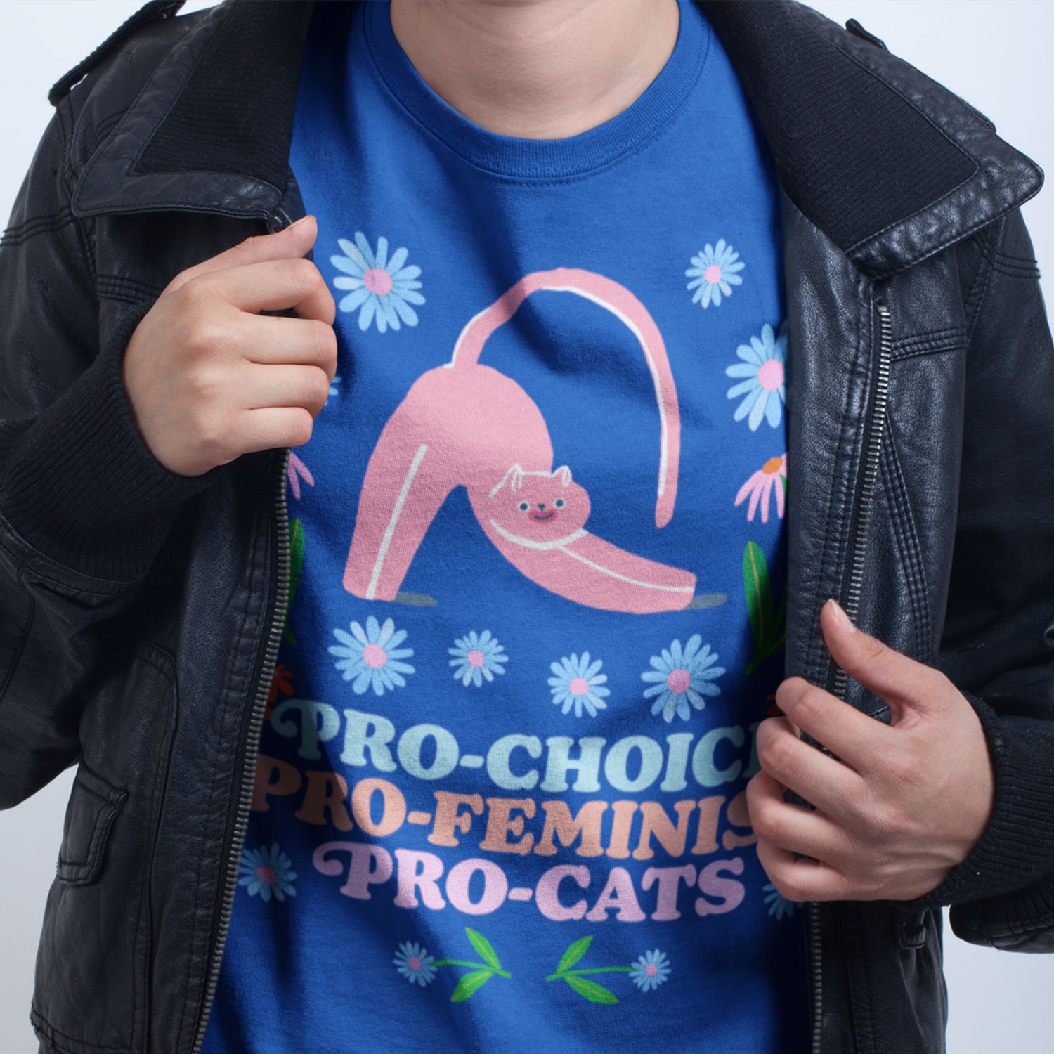 Woman wearing a blue Pro-Choice t-shirt with a pink cat graphic, holding a black leather jacket.