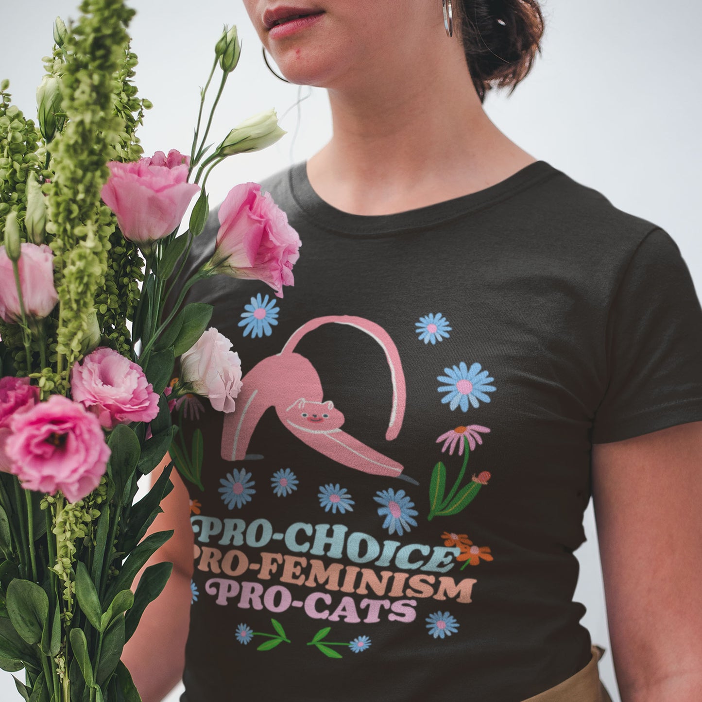 Woman wearing a black Pro-Choice t-shirt with a pink cat graphic, holding flowers.