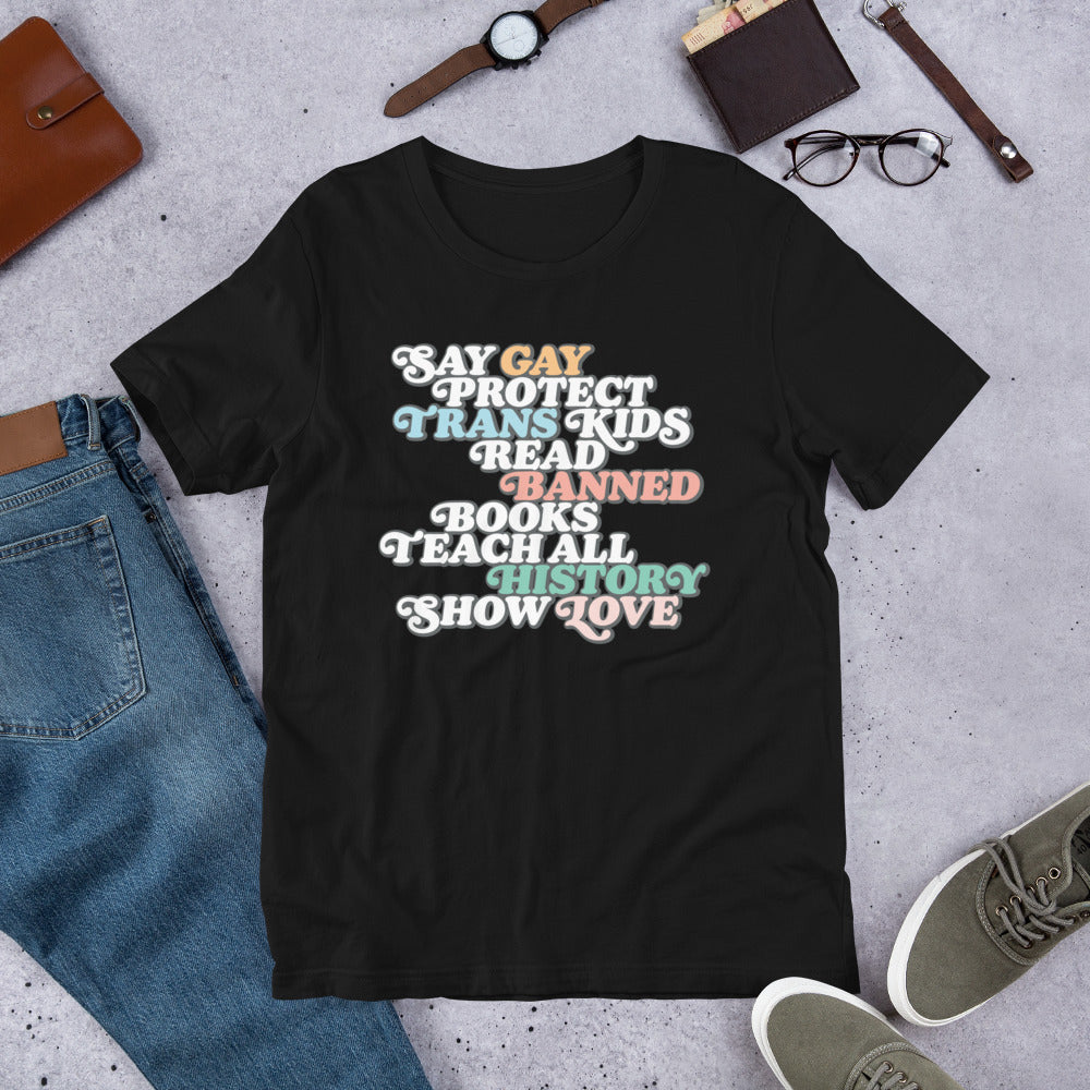 Flat lay of the "Say Gay Protect Trans Kids Read Banned Books Teach All History Show Love" Unisex T-Shirt with bold graphic.
