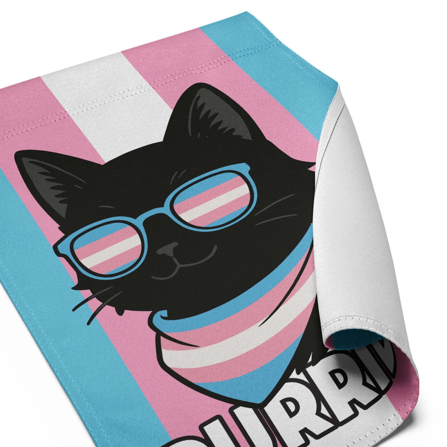Close-up of the “Purride” Trans Pride cat garden flag, showing curled fabric edge with black cat design and transgender pride colors.
