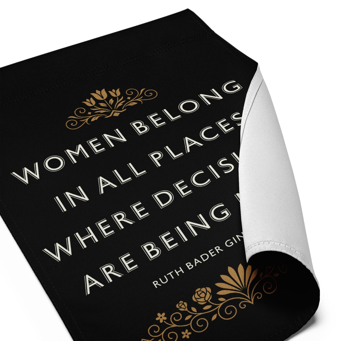 Close-up of the “Women Belong In All Places Where Decisions Are Being Made” RBG garden flag with curled edge showing gold decorative design.