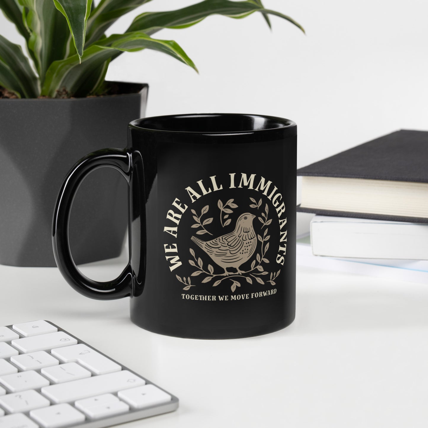 Close-up of linocut dove and leaves design with 'We Are All Immigrants' phrase on black mug.