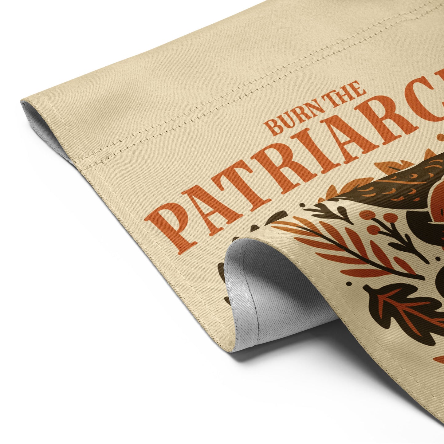 Close-up of rolled beige fabric showing the dragon’s tail and pumpkin detail from the “Burn the Patriarchy” feminist garden flag design.