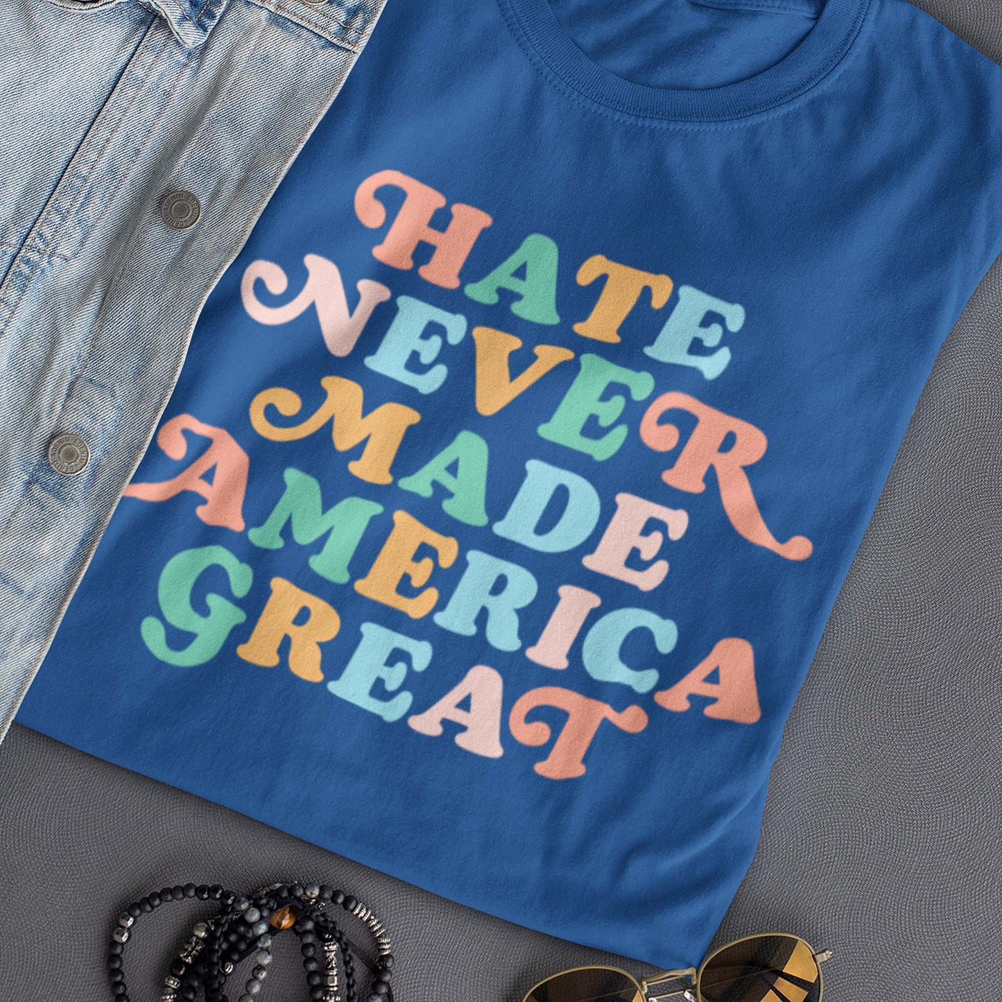 Blue “Hate Never Made America Great” t-shirt folded flat with retro multicolor text design.
