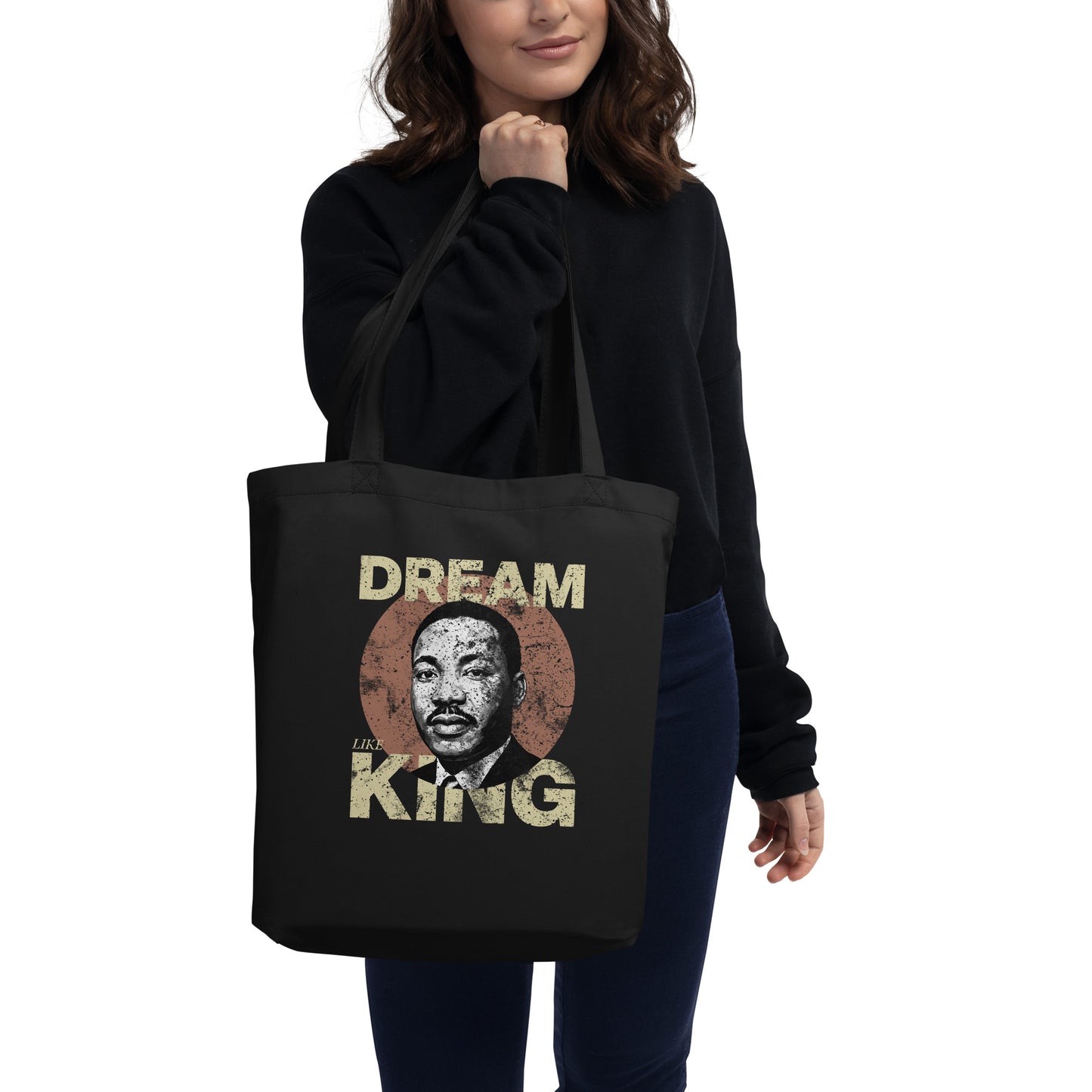 Woman holding a black eco tote bag printed with “DREAM LIKE KING” and Martin Luther King Jr.’s portrait inside a textured circle. Retro civil-rights design from Blue Wave USA.