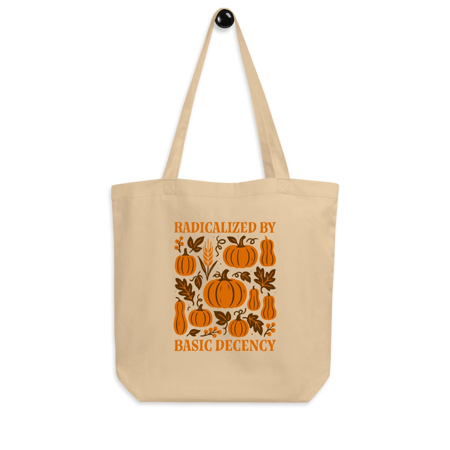 “Radicalized by Basic Decency” autumn pumpkin tote bag displayed hanging, seasonal progressive design for Thanksgiving or everyday use.