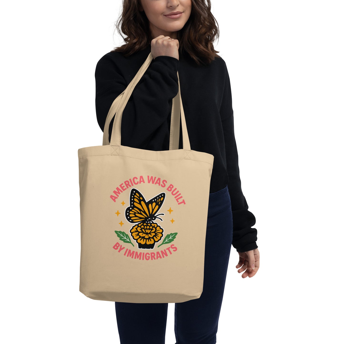 Model carrying natural “America Was Built by Immigrants” eco tote bag with butterfly and flower art. Pro-immigrant rights design by Blue Wave USA.