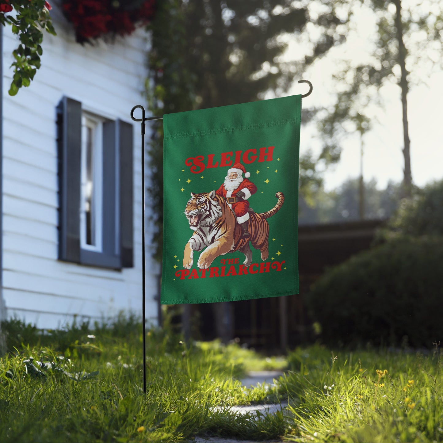 Feminist Christmas garden flag with Santa riding a tiger and slogan “Sleigh the Patriarchy,” shown outdoors in front of a house.