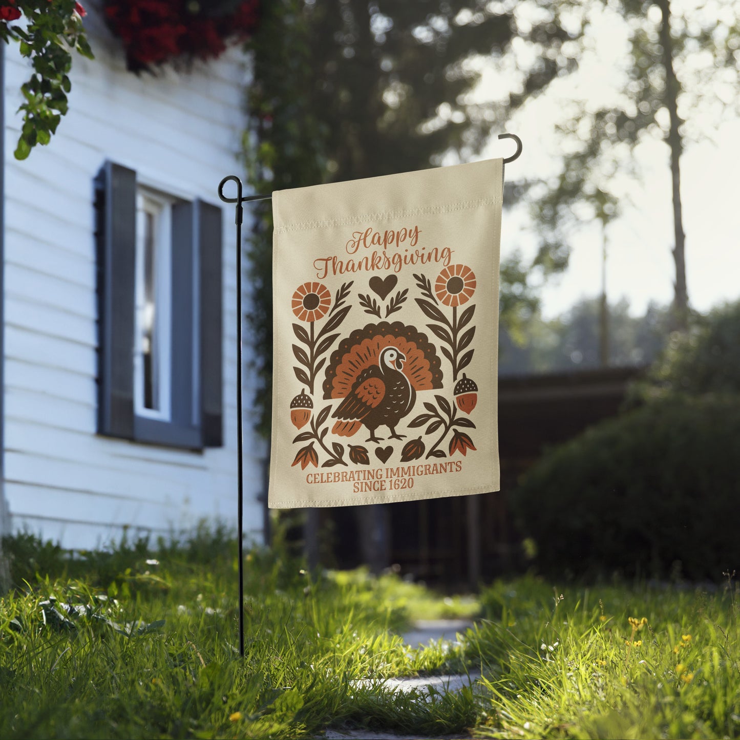 Thanksgiving garden flag reading “Happy Thanksgiving – Celebrating Immigrants Since 1620” with rustic turkey design, displayed on a flag stand in front of a house.