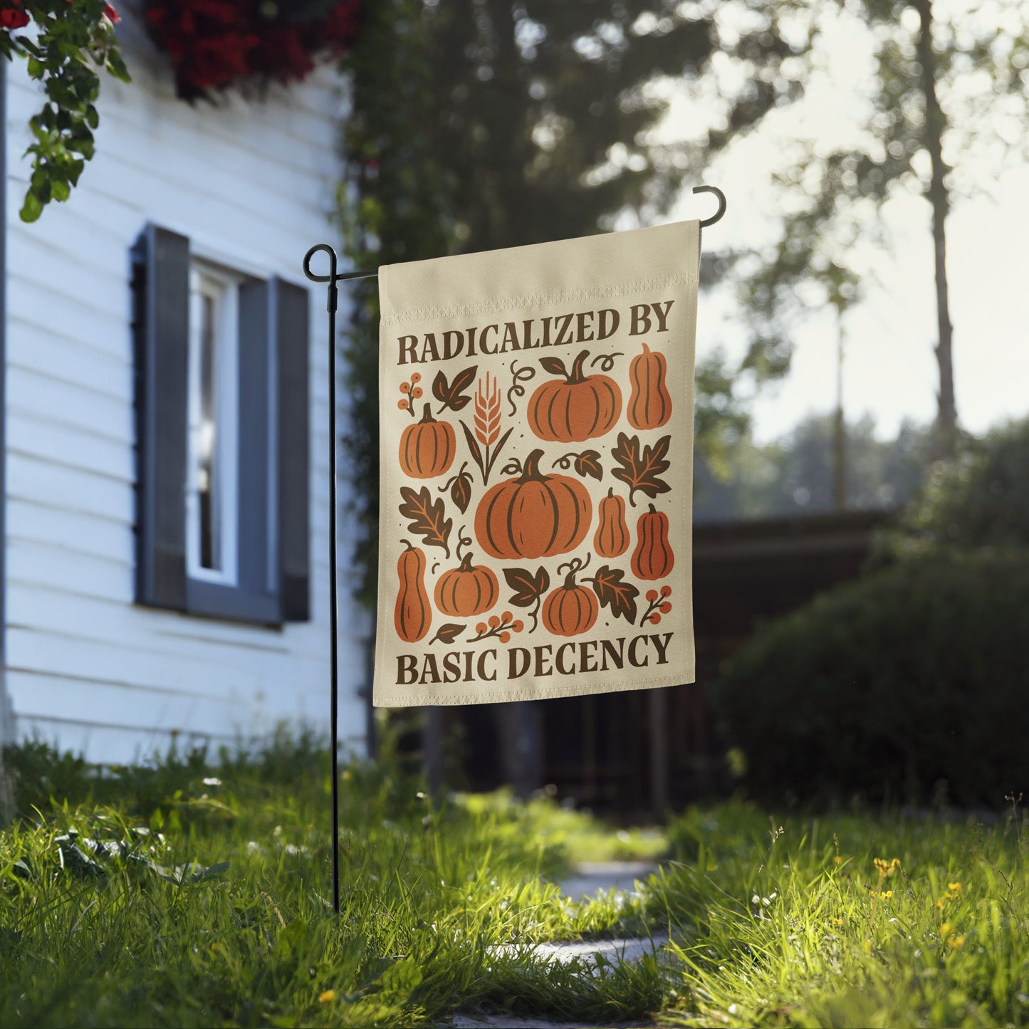 Progressive Thanksgiving garden flag reading “Radicalized By Basic Decency” shown on a flag stand in a front yard with pumpkins.