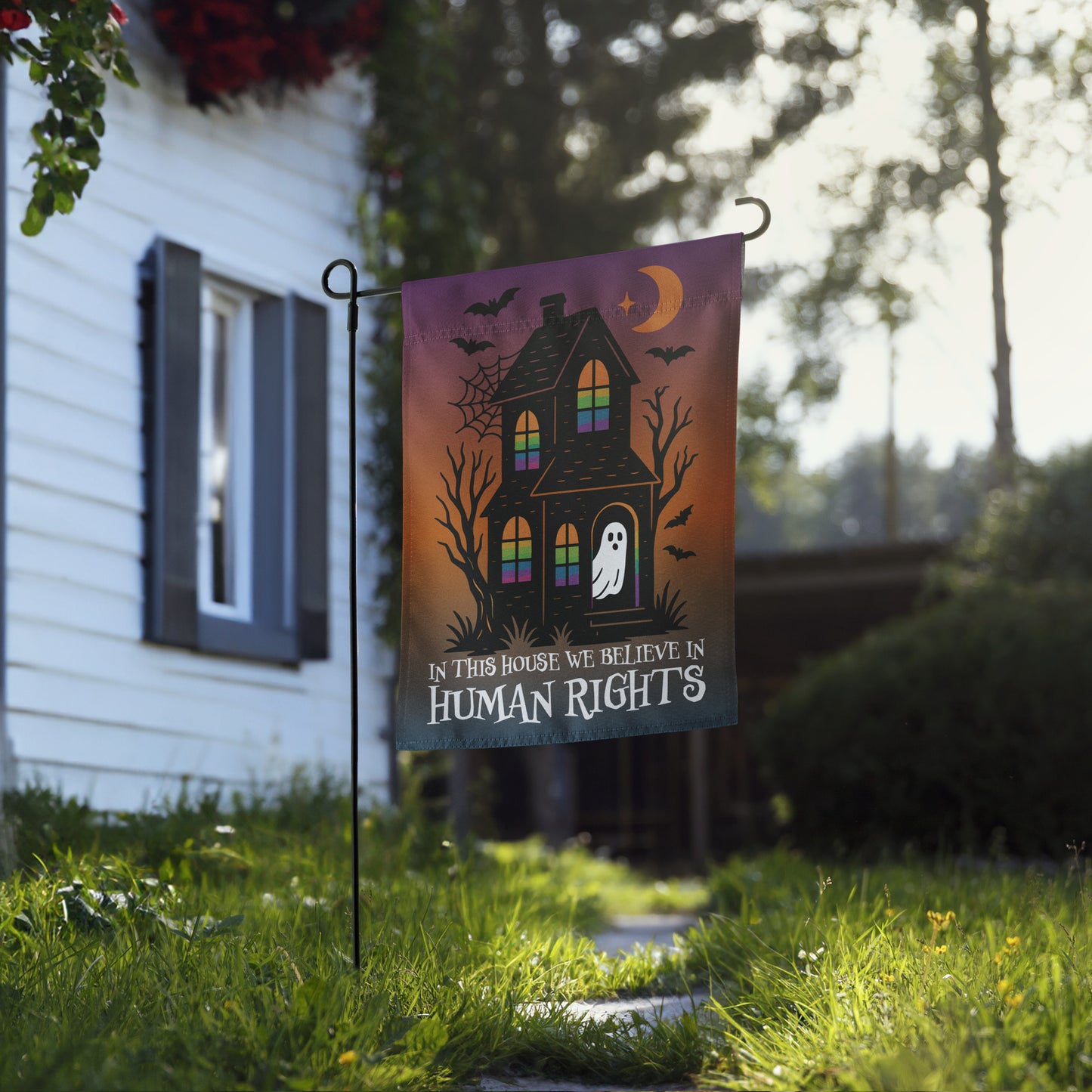 Progressive Halloween garden flag with haunted house and ghost design, shown on a flag stand in front of a home.