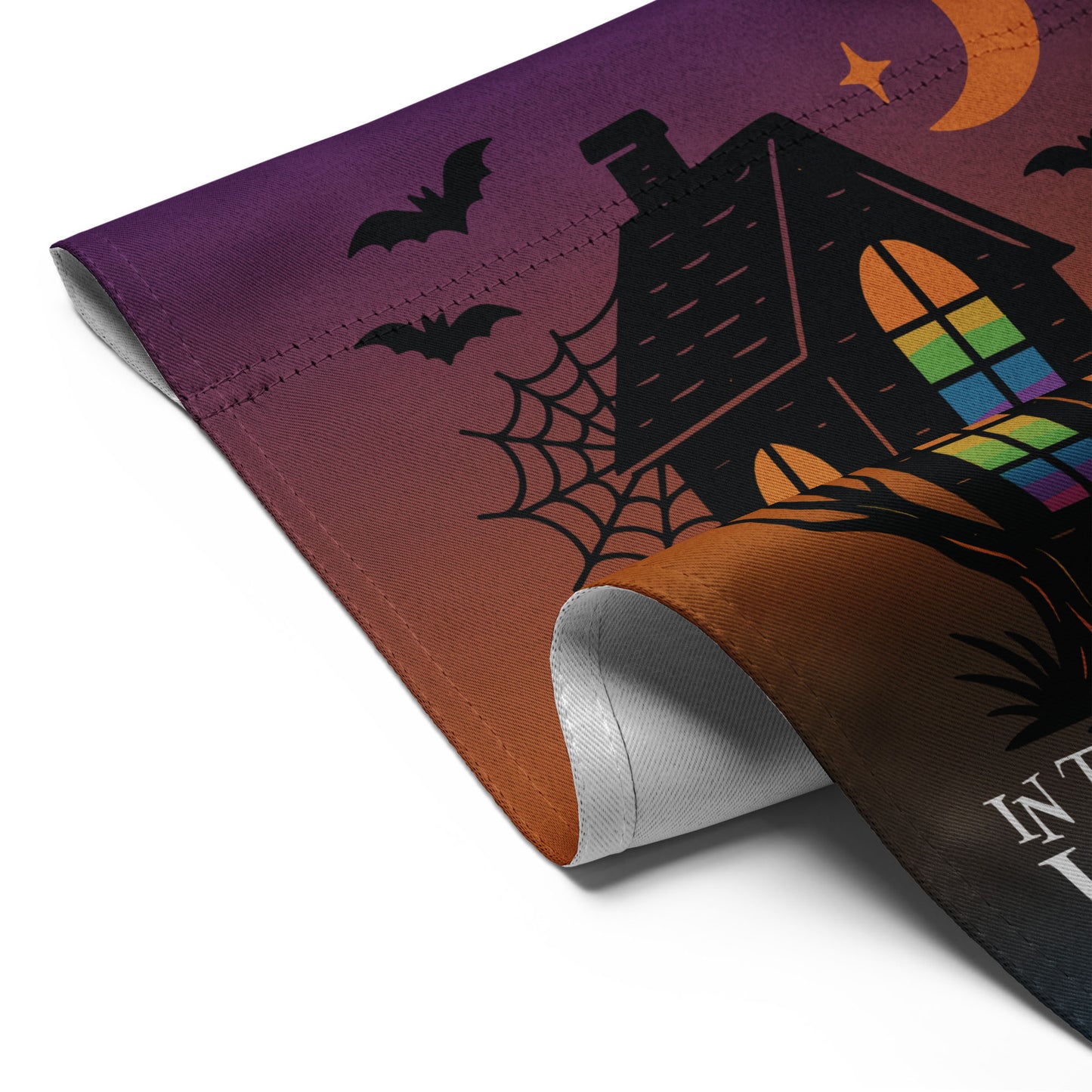 Close-up of the “In This House We Believe in Human Rights” Halloween flag with curled edge showing haunted house, tree branches, and bats.