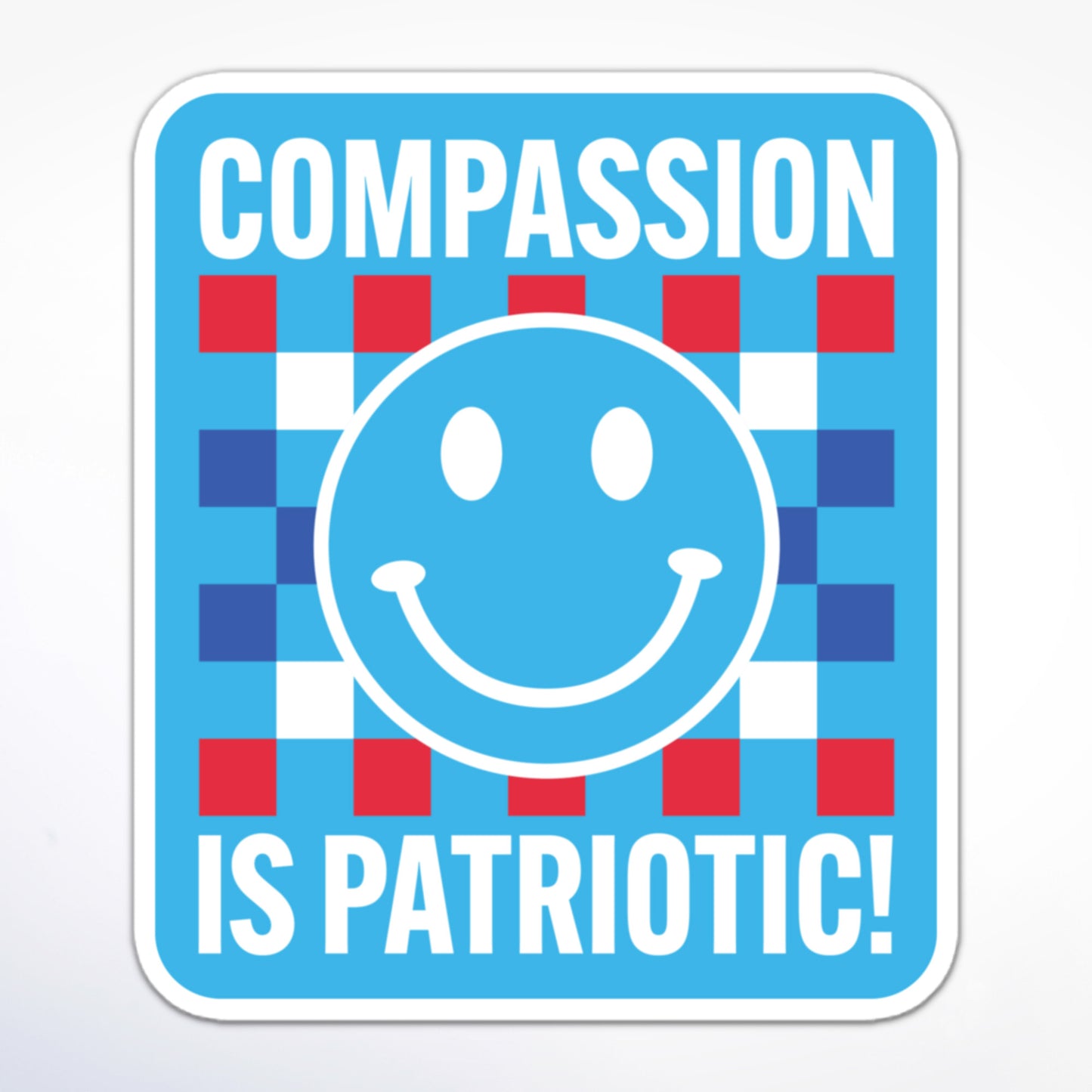 Social justice sticker with a blue smiley face, checkered pattern, and patriotic colors, displaying the message “Compassion is Patriotic!” in white block text.