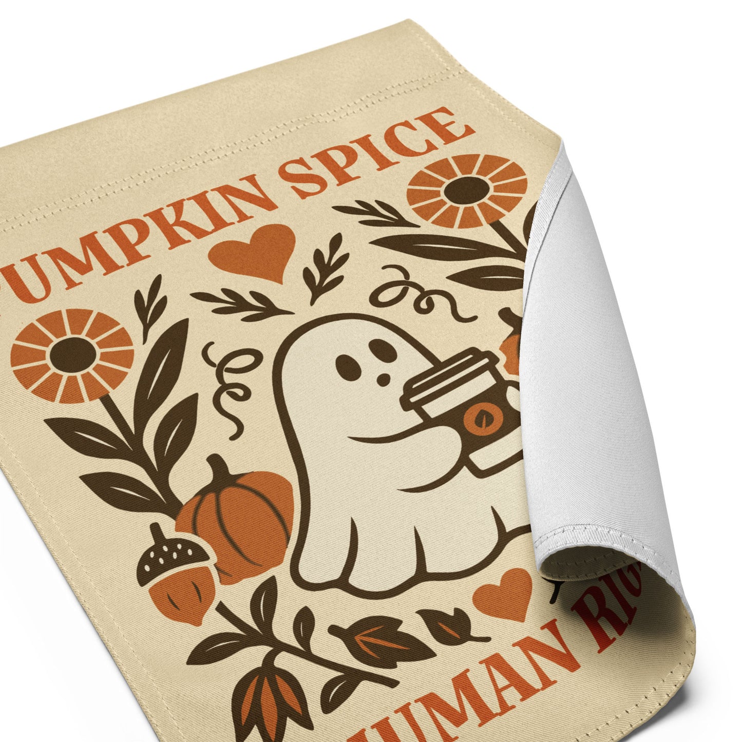 Close-up angled view of the “Pumpkin Spice & Human Rights” garden flag with curled fabric edge showing ghost, pumpkins, and floral artwork.