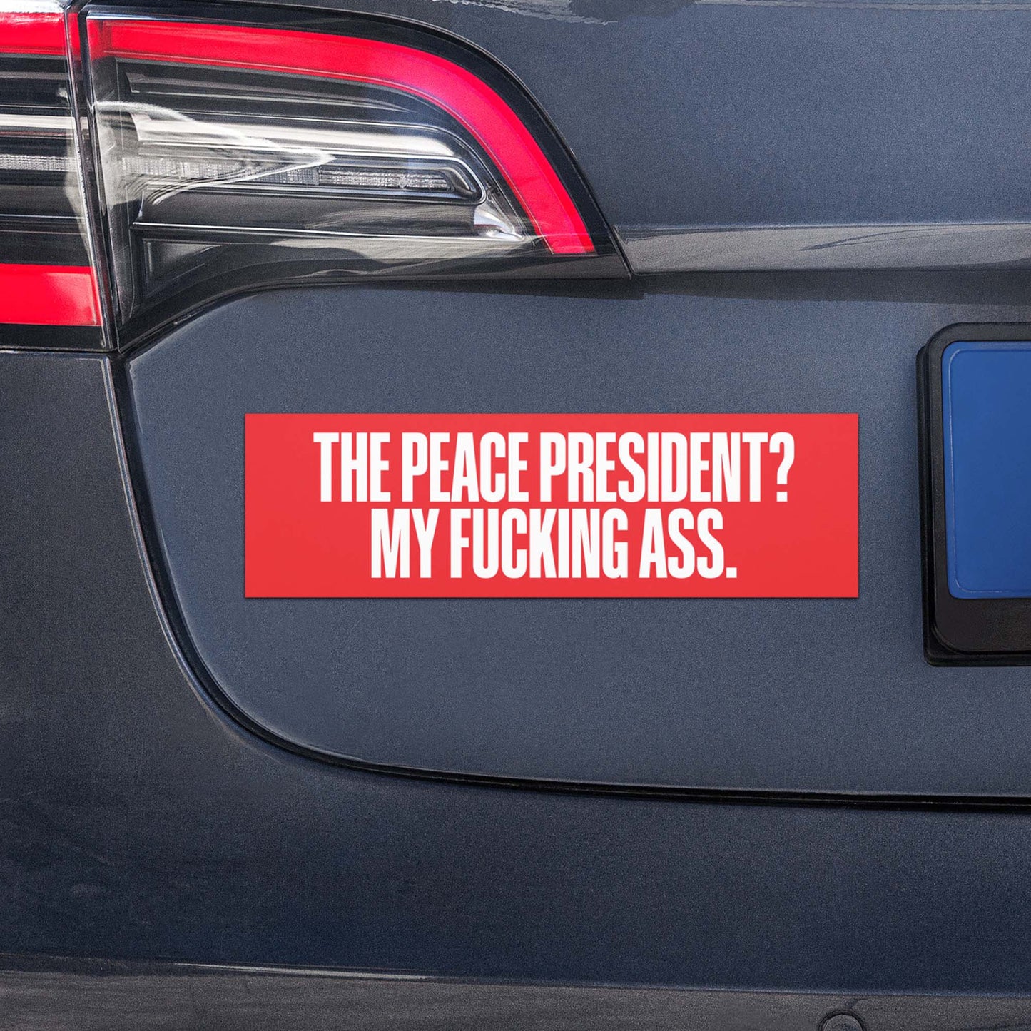 Car magnet displayed on vehicle bumper with bold white text reading “THE PEACE PRESIDENT? MY FUCKING ASS.” on red background. Anti-Trump Car Magnet by Blue Wave USA.