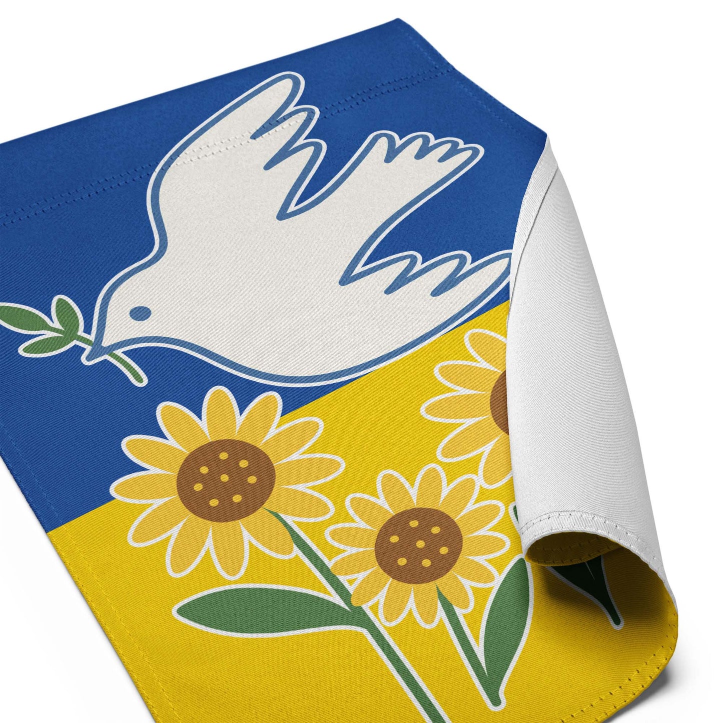 Angled close-up view of the Ukraine Solidarity garden flag with curled corner showing sunflower and blue sky background.
