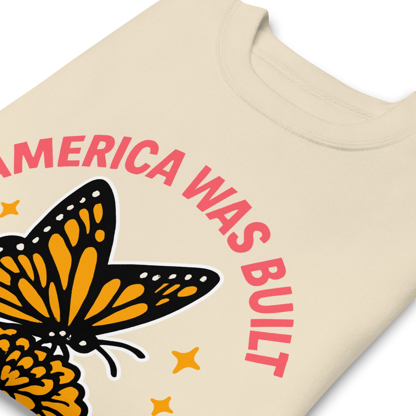 Close-up of embroidered monarch butterfly and red text reading “America Was Built by Immigrants,” progressive design detail for equality advocates.