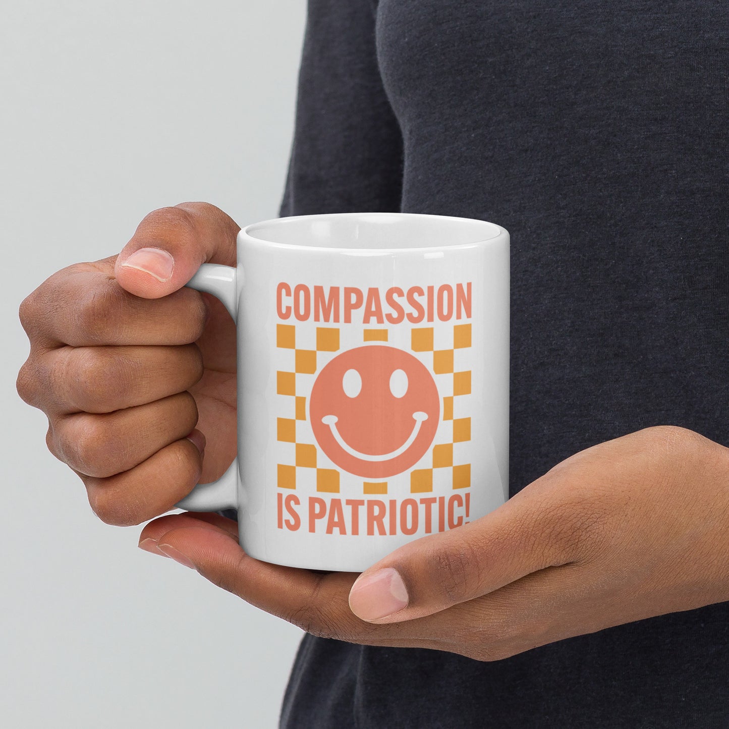 Front view of the 11 oz Compassion Is Patriotic Smiley Face White Mug featuring a cheerful smiley and bold message.