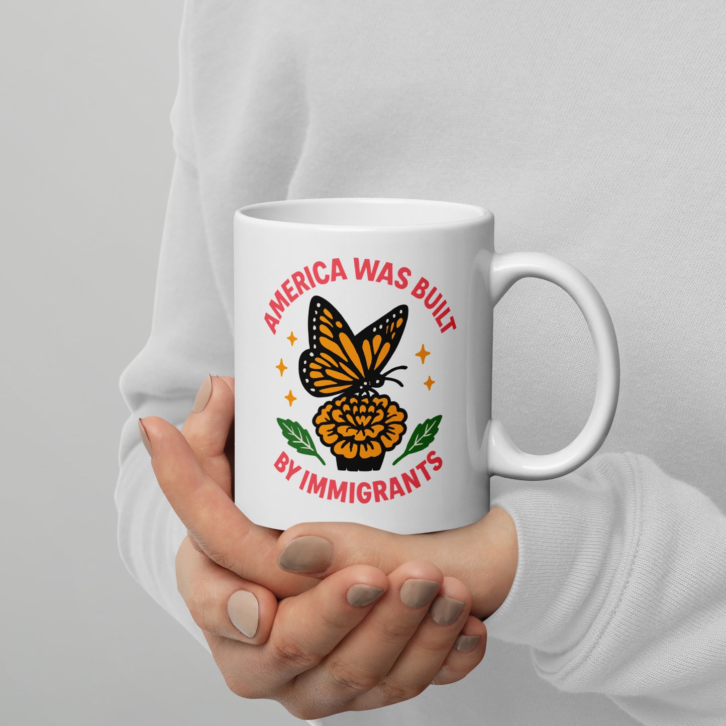 Person holding 11 oz “America Was Built by Immigrants” monarch butterfly mug, Blue Wave USA progressive drinkware for equality advocates.