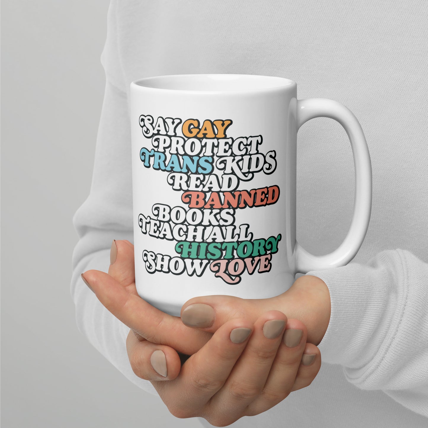 Mug Lifestyle Image: 15 oz "Say Gay Protect Trans Kids Read Banned Books Teach All History Show Love" Mug held by the model