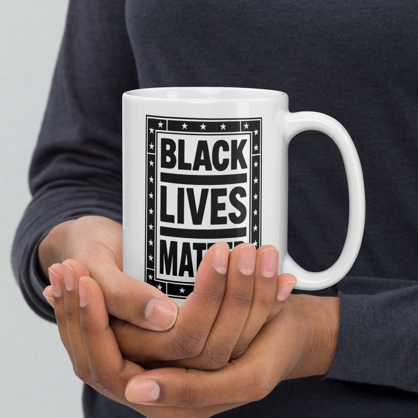 Person holding a white 15 oz ceramic mug displaying the framed black-and-white “BLACK LIVES MATTER” design, strong contrast and star detailing supporting a civil rights message from Blue Wave USA.