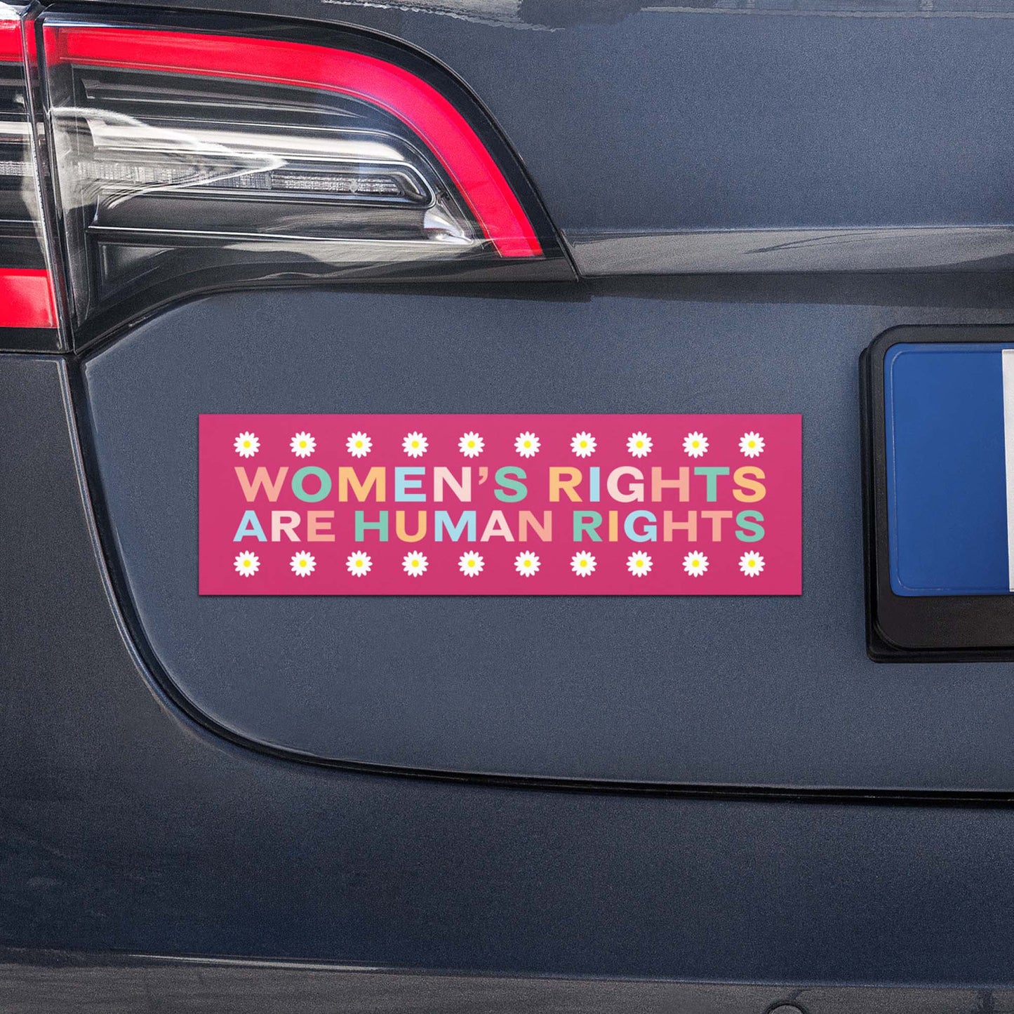 Pink bumper magnet with daisy pattern and the phrase “WOMEN’S RIGHTS ARE HUMAN RIGHTS” displayed on vehicle trunk.