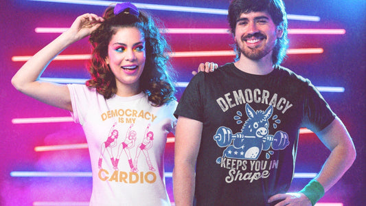Man and woman modeling 1980s retro-style "Democracy" themed graphic t-shirts with fitness-inspired illustrations and neon backgrounds.