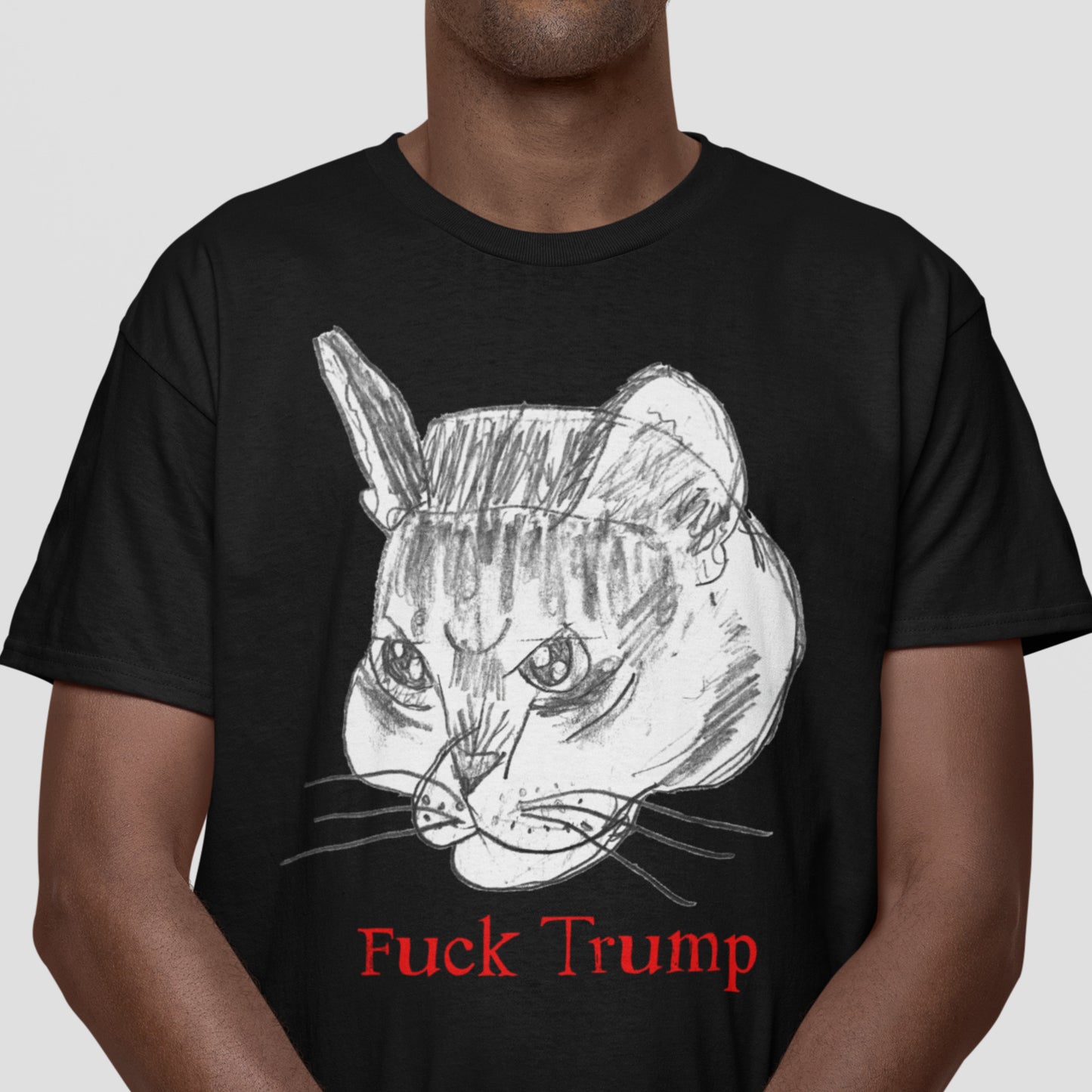 Model wearing black unisex t-shirt with sketched cat face illustration and red text reading “Fuck Trump,” casual studio lighting.