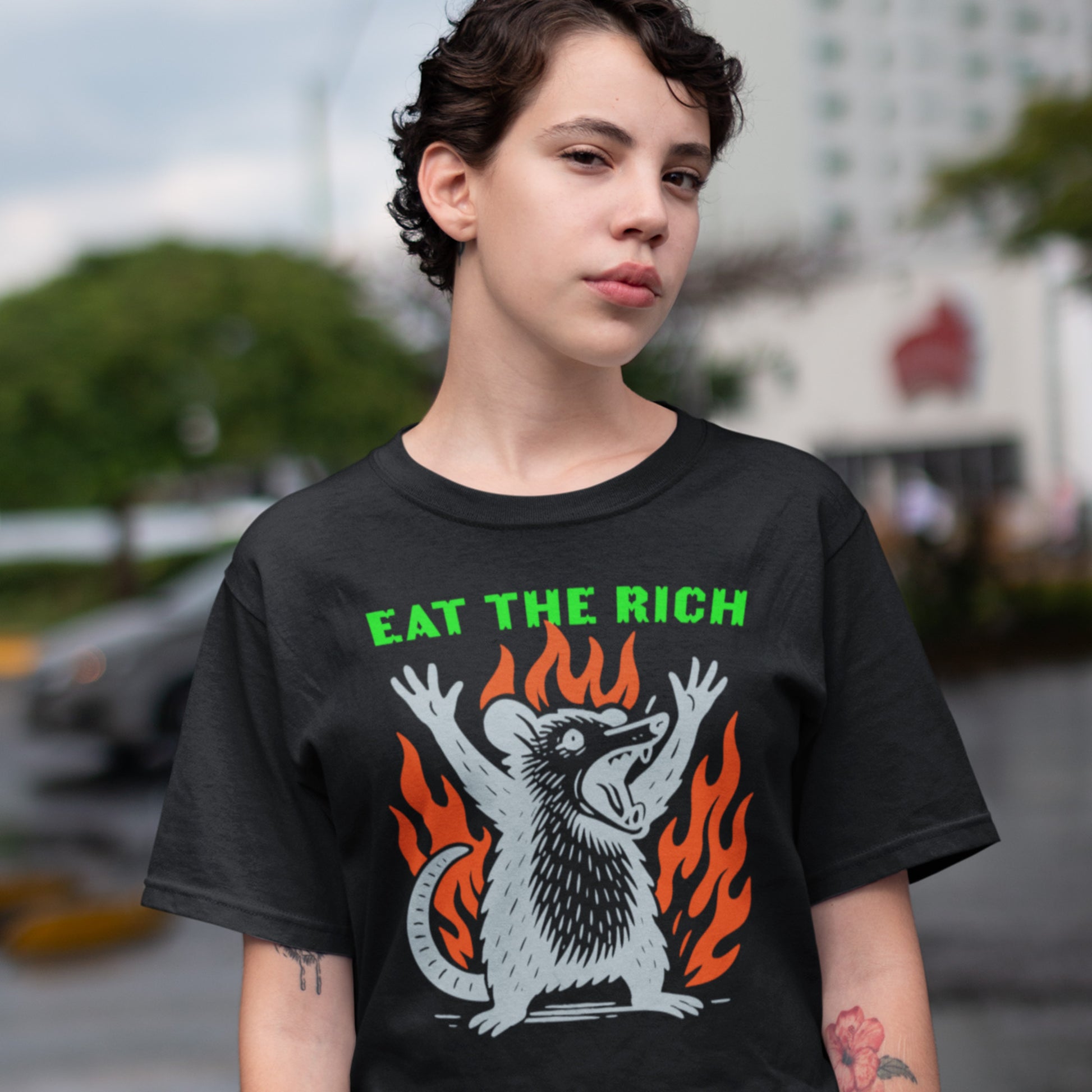 Model wearing black unisex t-shirt featuring flaming punk opossum illustration and bold “Eat The Rich” anti-capitalist protest message.