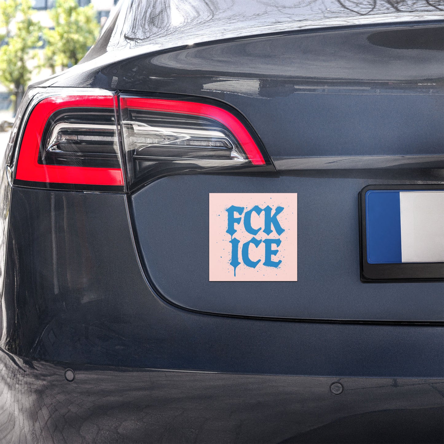 Car magnet displayed on rear of vehicle showing blue “FCK ICE” gothic lettering on pink background with speckled accents, anti-ICE design from Blue Wave USA.