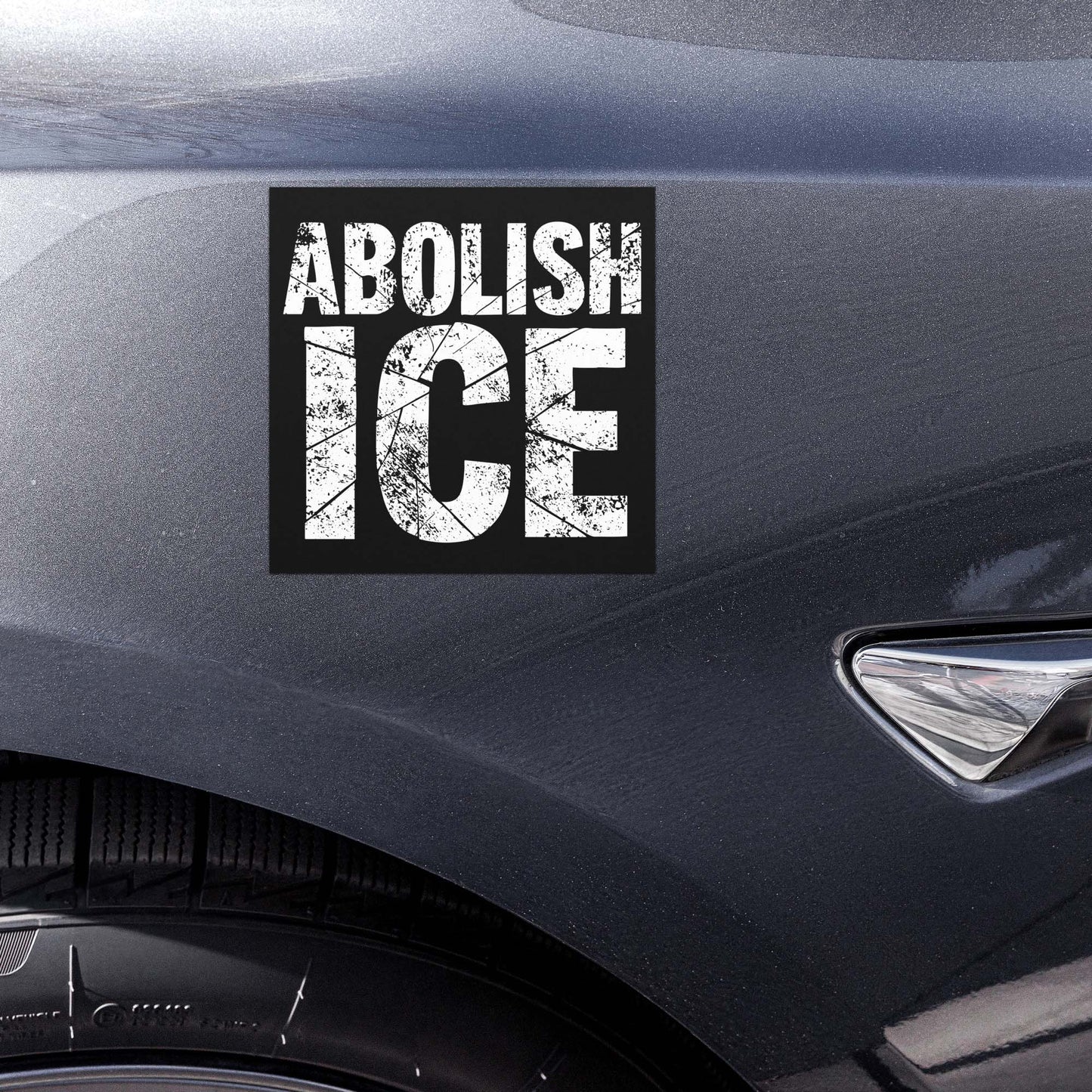 Car magnet displayed on vehicle door featuring bold distressed white lettering on black background, stacked text layout, printed message “ABOLISH ICE,” activist car magnet from Blue Wave USA.