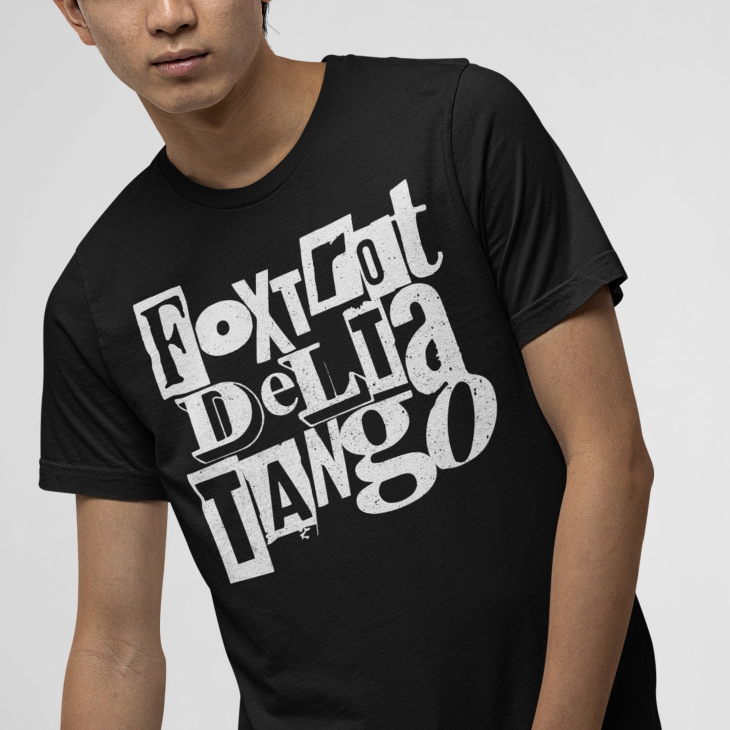 Model wearing black unisex t-shirt with stacked white block lettering reading “Foxtrot Delta Tango,” casual pose, neutral indoor background.