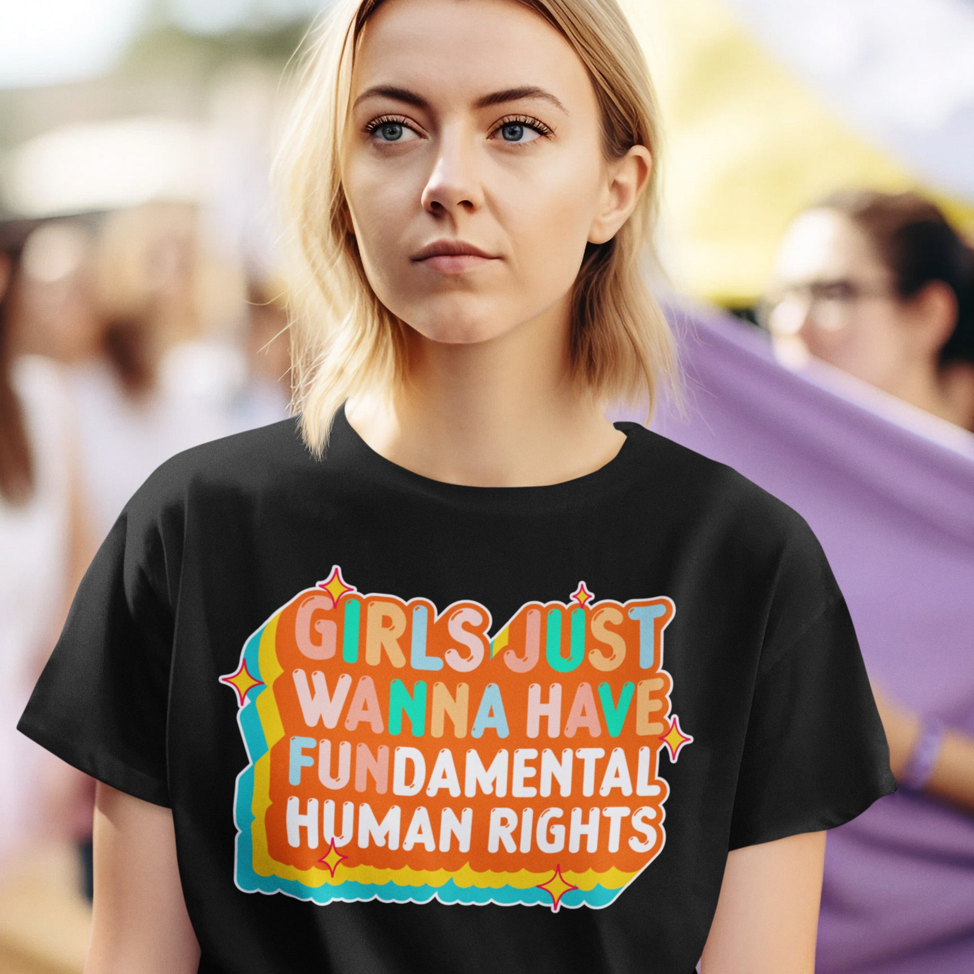 Model wearing the black “Girls Just Wanna Have Fundamental Human Rights” retro sunset design t-shirt in a casual streetwear look. Progressive fashion by Blue Wave USA.
