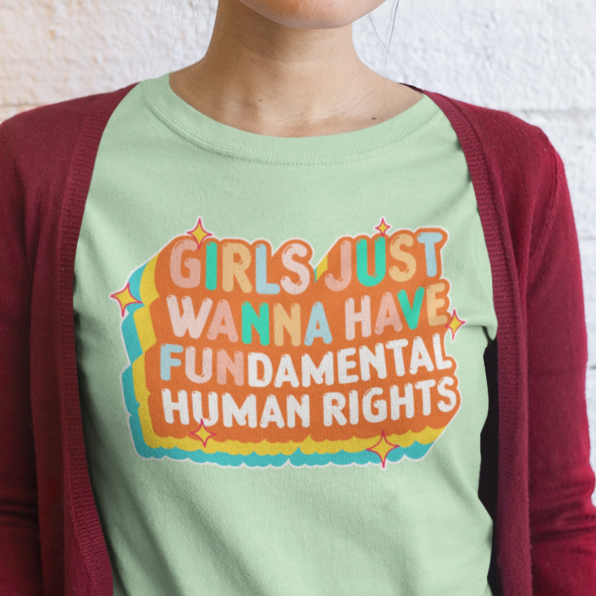 Model wearing mint “Girls Just Wanna Have Fundamental Human Rights” t-shirt layered with a red cardigan. Bright retro feminist tee by Blue Wave USA.