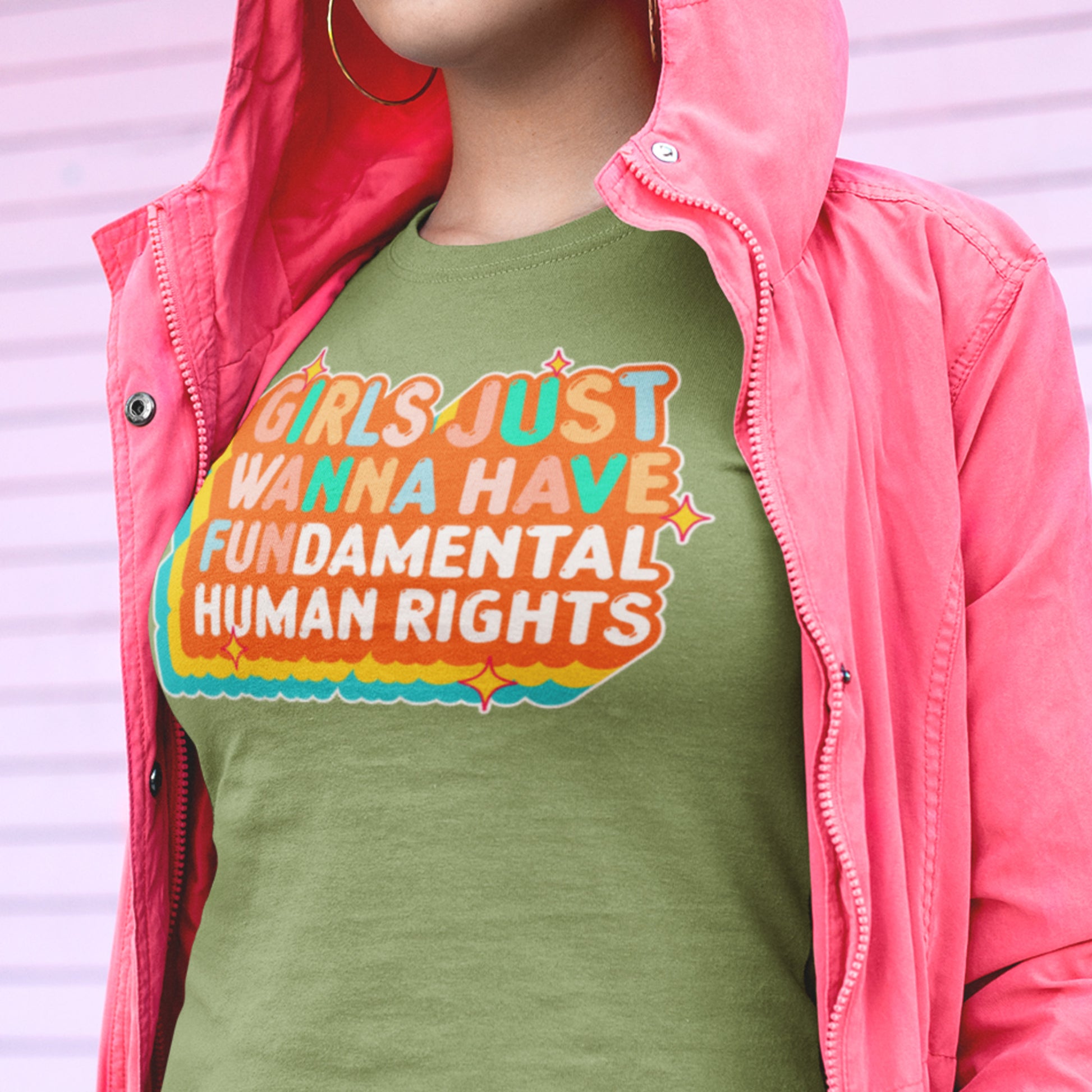 Model wearing the leaf green “Girls Just Wanna Have Fundamental Human Rights” t-shirt layered under a pink jacket. Retro feminist statement tee by Blue Wave USA.