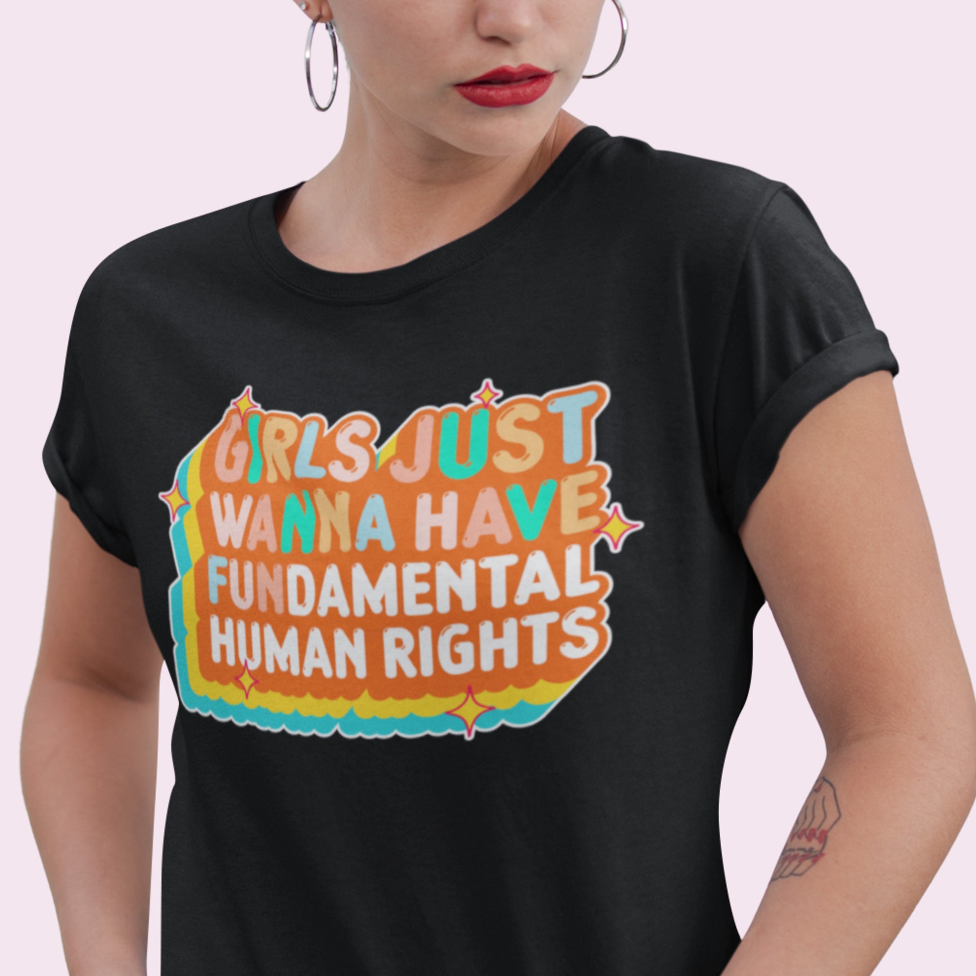 Model in black “Girls Just Wanna Have Fundamental Human Rights” t-shirt with orange-and-teal groovy retro text. Stylish activism look by Blue Wave USA.