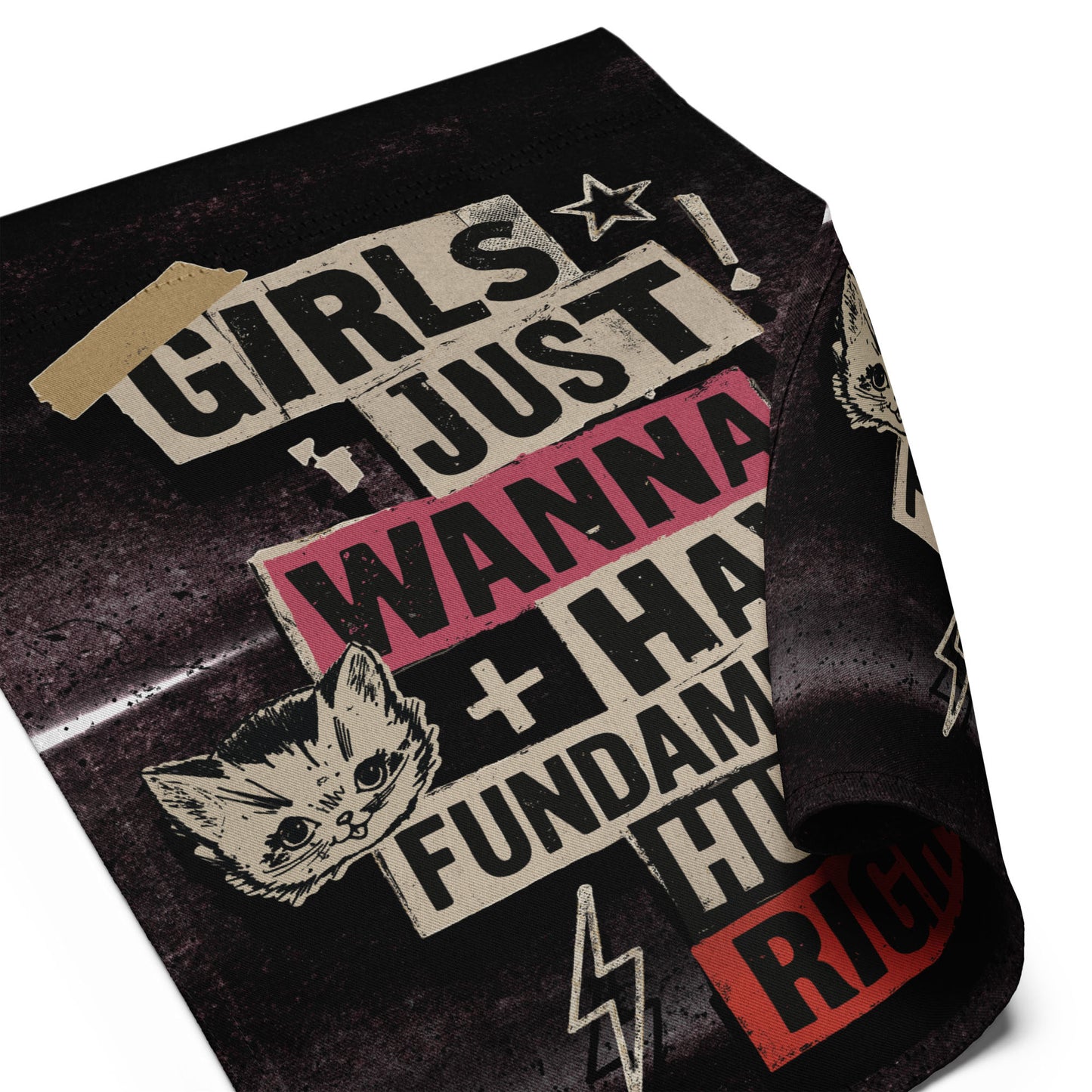 Angled close-up of the garden flag fabric showing bold punk lettering, lightning bolt details, and distressed textures reading “GIRLS JUST WANNA HAVE FUNDAMENTAL HUMAN RIGHTS,” by Blue Wave USA.