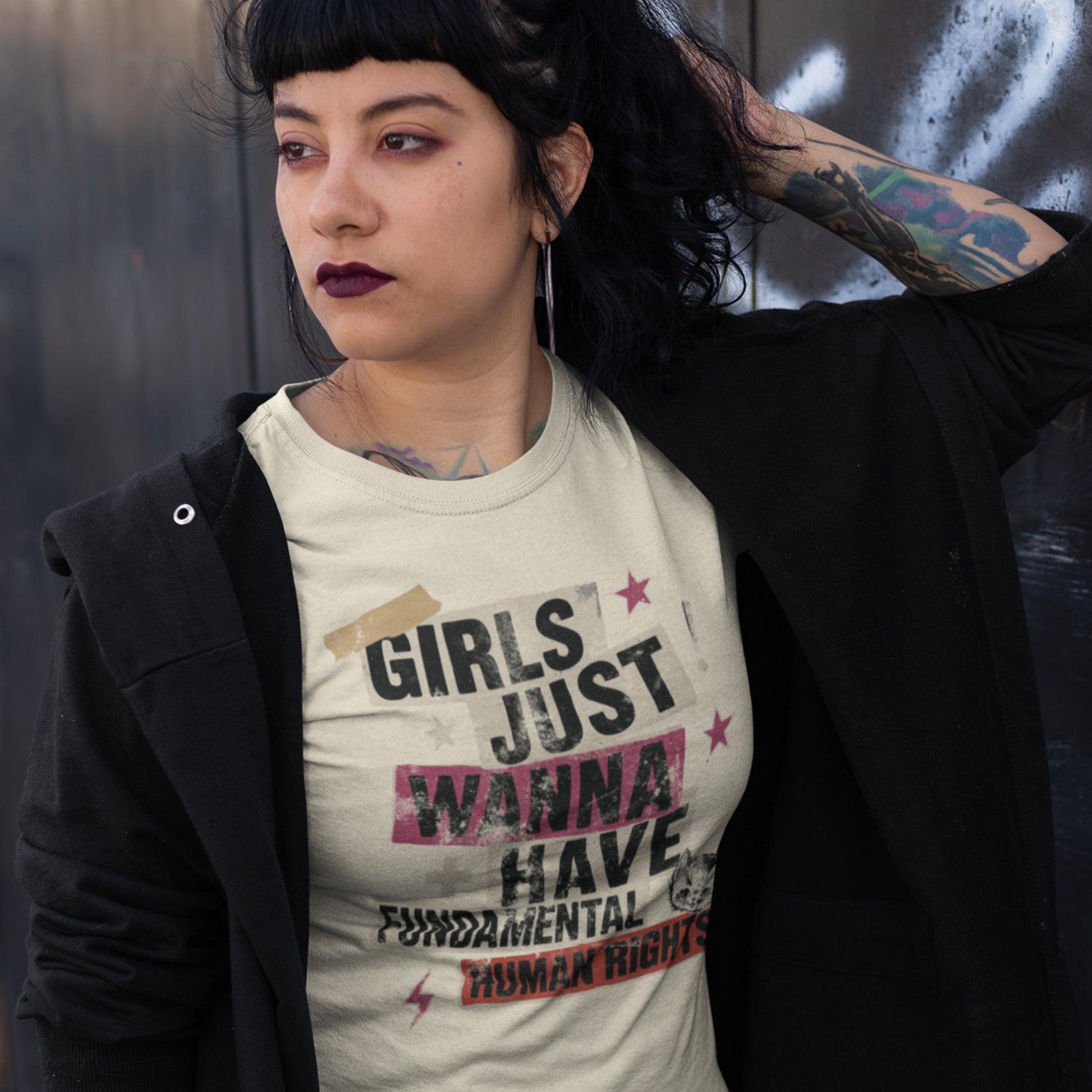 Model wearing cream “Girls Just Wanna Have Fundamental Human Rights” punk collage t-shirt layered under a black jacket. Edgy feminist style by Blue Wave USA.