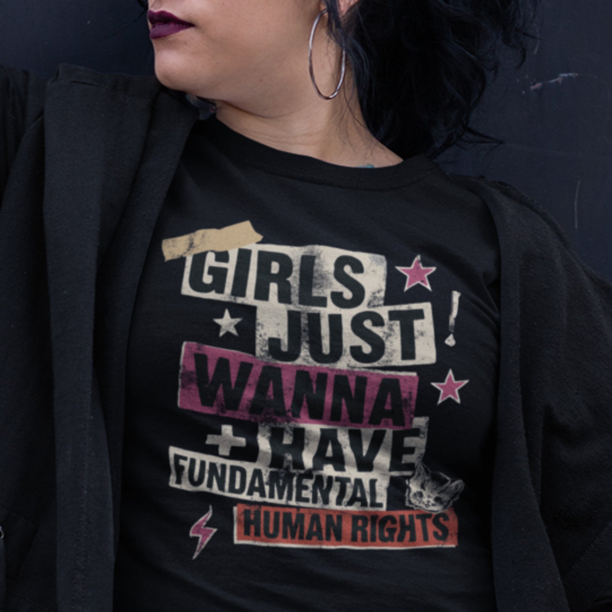 Model styled in a black “Girls Just Wanna Have Fundamental Human Rights” shirt with distressed collage lettering and star graphics. Rebellious and empowering streetwear for activists.