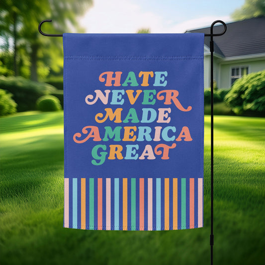 “Hate Never Made America Great” garden flag with bold retro lettering in rainbow colors and striped border, displayed outdoors on a flagpole.