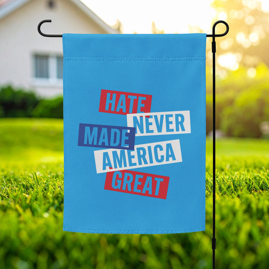 Progressive garden flag featuring stacked typographic artwork and phrase “HATE NEVER MADE AMERICA GREAT,” blue background, displayed outdoors on metal garden stand.