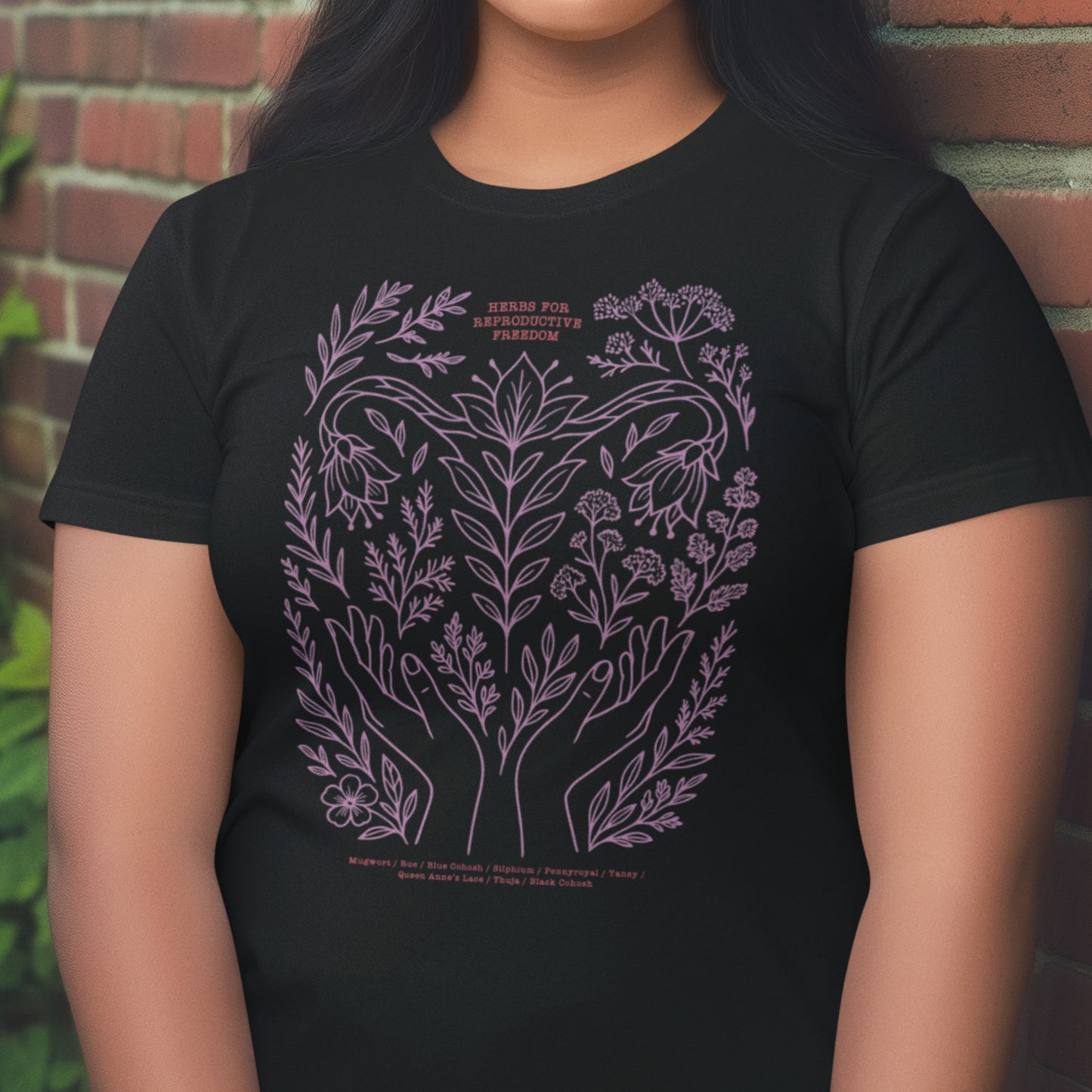 Model wearing black relaxed fit feminist t-shirt with lavender herbal illustration symbolizing care, healing, and reproductive autonomy.