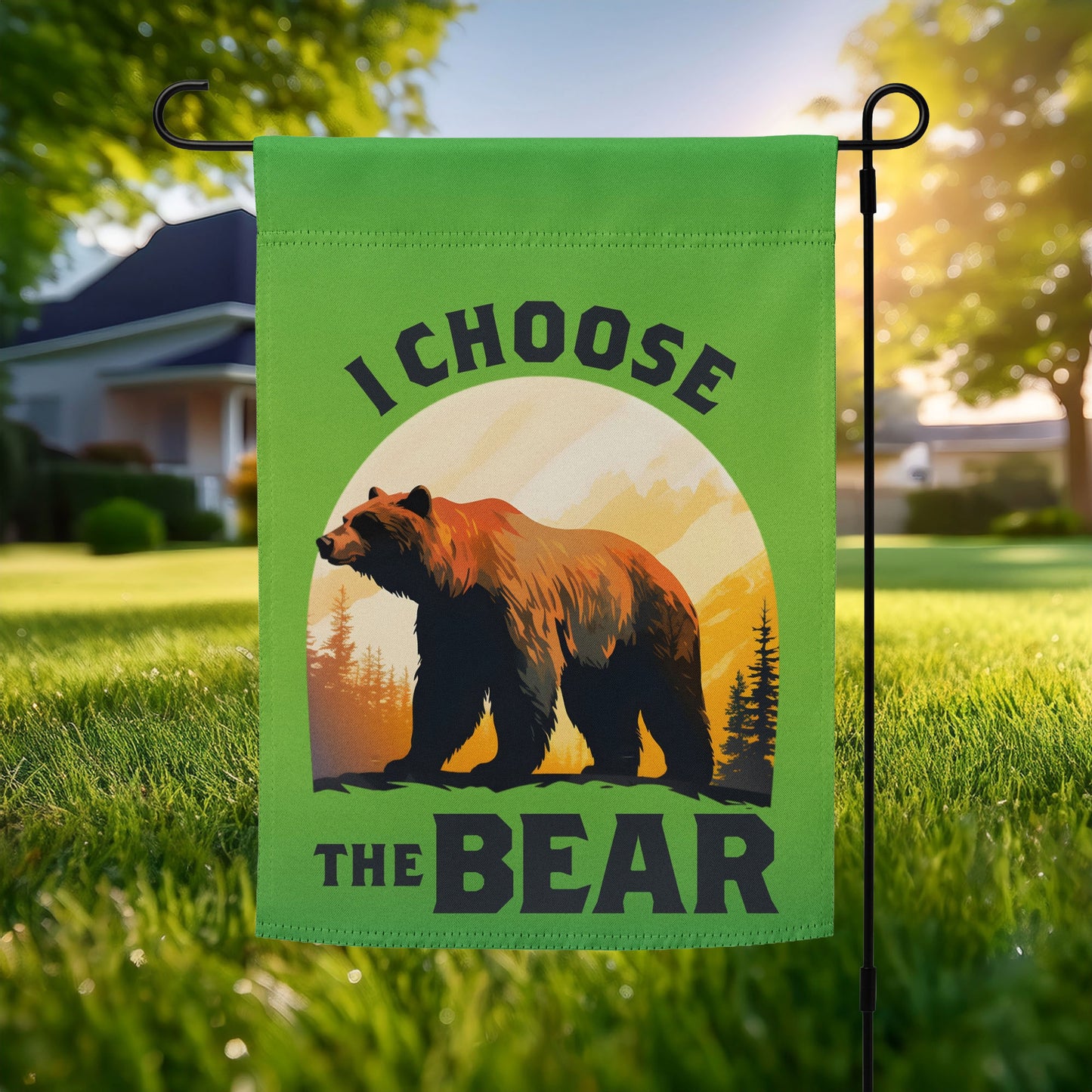Green garden flag displayed outdoors on a metal stand, featuring a realistic bear silhouette against a sunset landscape with trees and bold text reading “I CHOOSE THE BEAR.”