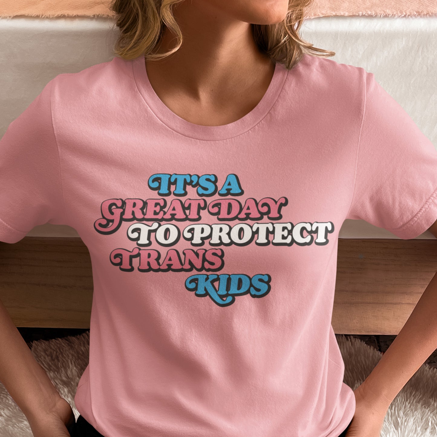 Model wearing trans rights T-shirt featuring pastel typography and the phrase “It’s A Great Day To Protect Trans Kids” supporting transgender youth.